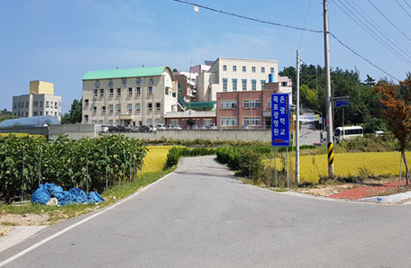 파란색 안내판 뒤로 이어져 있는 길 끝에 광명원 건물 서 있는 모습