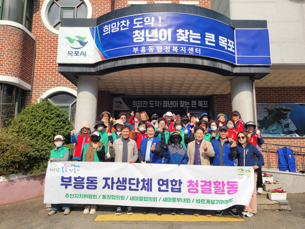 부흥동 자생단체 회원들이 거리와 인도 주변에서 쓰레기를 줍는 등 청결활동을 진행하고 있는 모습. 빨간 조끼를 입은 10여명의 참여자들이 나무 밑과 보도블록 위에서 적극적으로 환경정화 활동 중이다. 앞쪽에 있는 여성은 풀밭에 쓰레기를 목장갑이 낀 손으로 수거하는 모습이며 뒤편에는 집게를 이용해 쓰레기를 줍는 여러참가자들의 모습이 보인다.