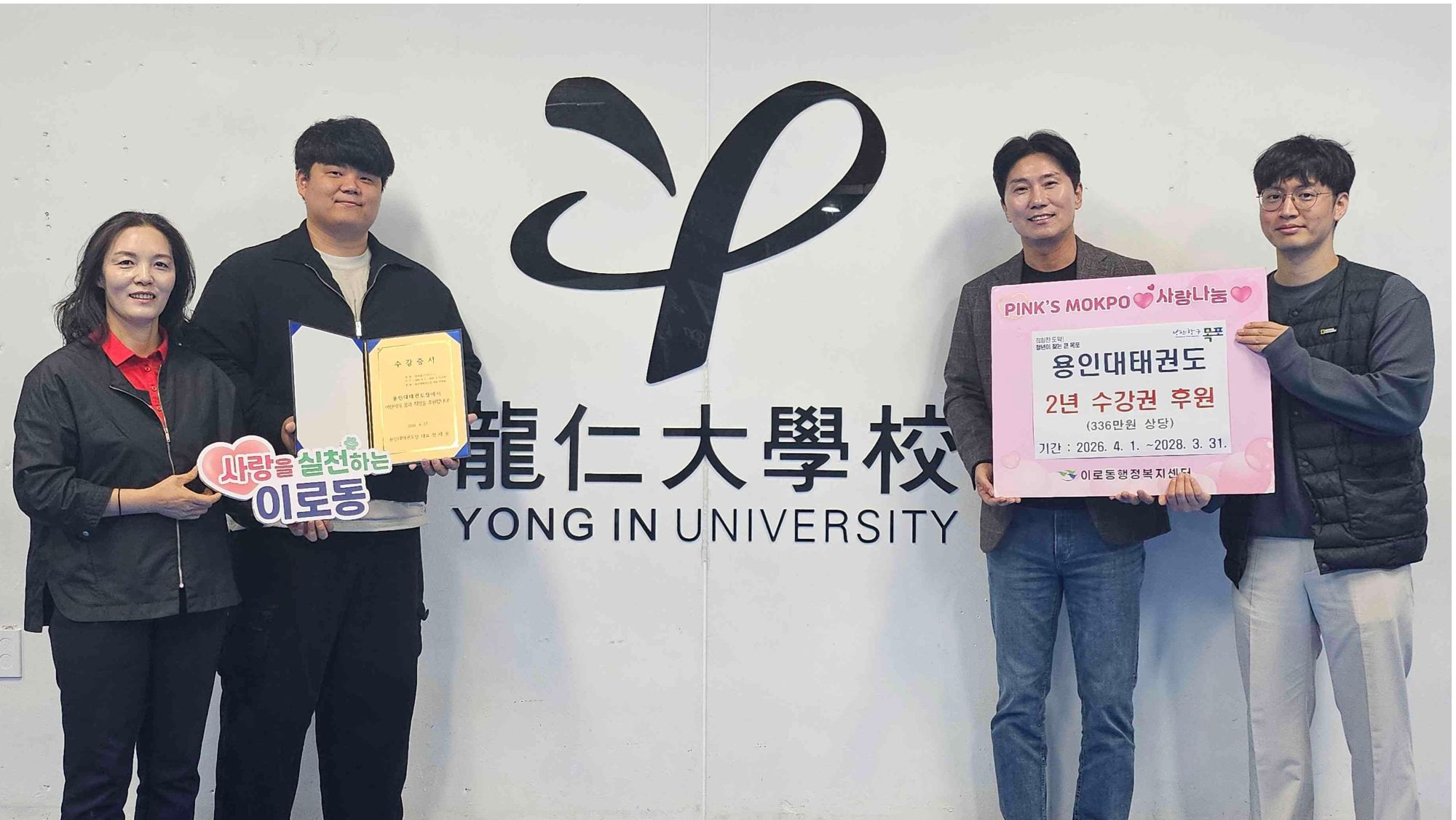 왼쪽에 사랑을 실천하는 이로동 문구를 들고 있는 중년 여성과 후원증서를 들고 있는 남성이 있다. 오른쪽에 용인대태권도 2년 수강권 후원 문구가 적힌 팻말을 들고 있는 남성 두명이 있다.