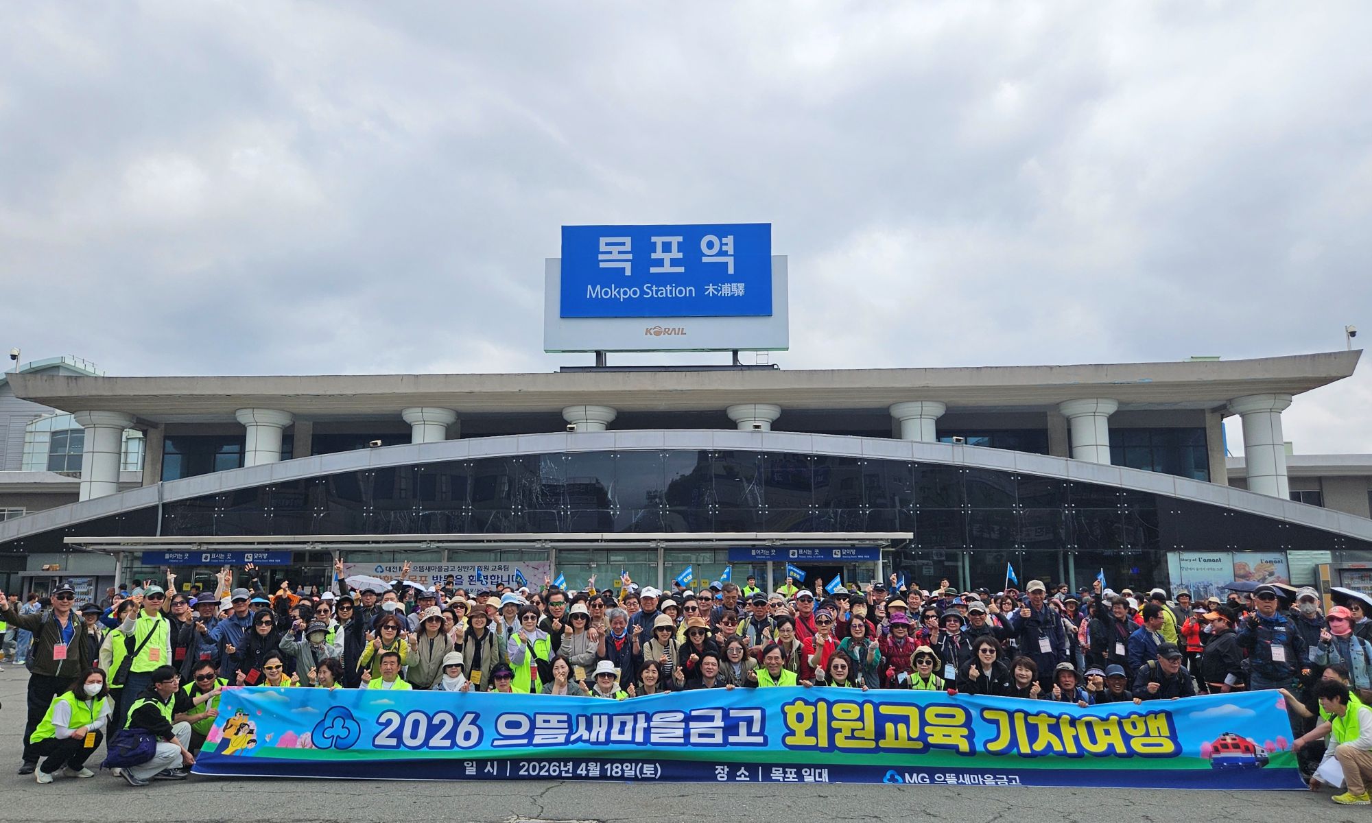 2026 으뜸새마을금고 회원교육 기차여행 일시|2026년 4월 18일 (토) 장소| 목포일대| MG으뜸새마을금고 문구가 적힌 현수막을 들고 목포역 앞에서 찍은 단체사진