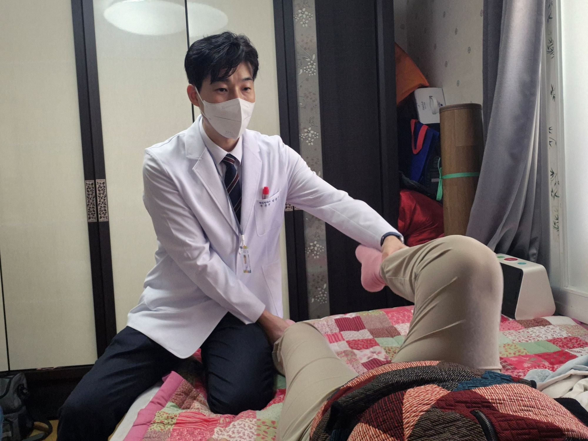 어르신 가정을 직접 방문한 의사가 누워 있는 어르신의 다리 관절을 살펴보고 있는 모습