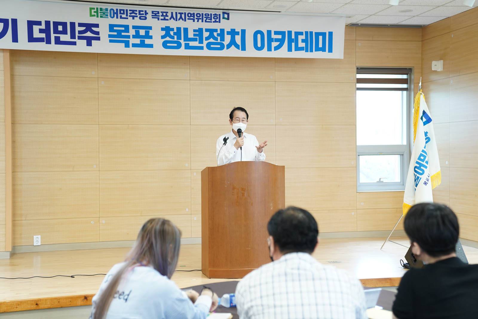 제1기 더민주 목포 청년정치 아카데미에서 연단에 서서 연설 중인 시장님 사진이다 우측에 더불어민주당 기가 걸려 있다