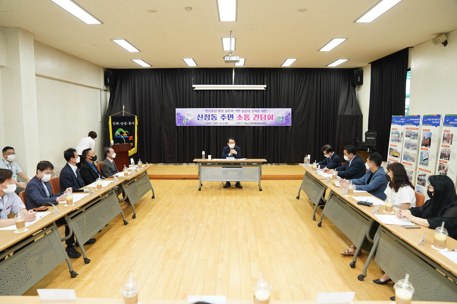 산정동 주민 소통 간담회 라고 적힌 현수막이 걸려 있다. 강당에서 시장님과 관계자들이 간담회를 하고 있는 사진이다.