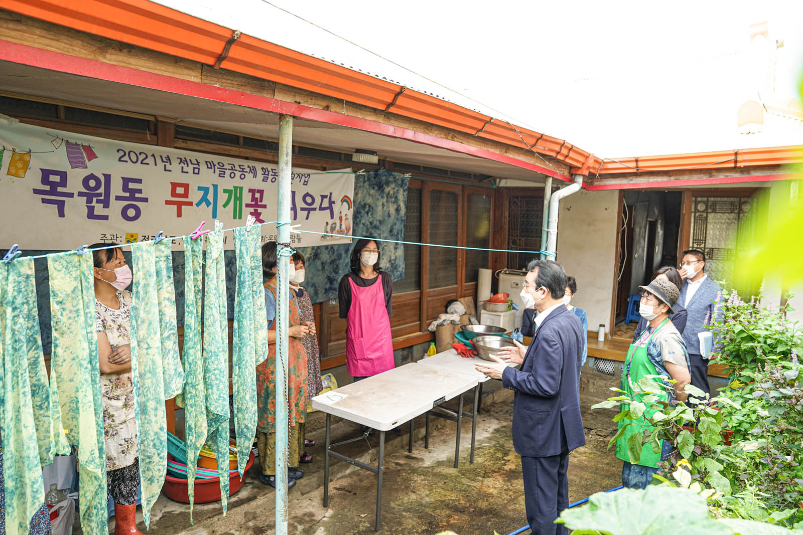 목원동 무지개꽃 피우다 라고 적힌 현수막이 걸려 있는 곳에서 관계자들이 서 있고 그 앞에 시장님이 이야기를 하고 있다