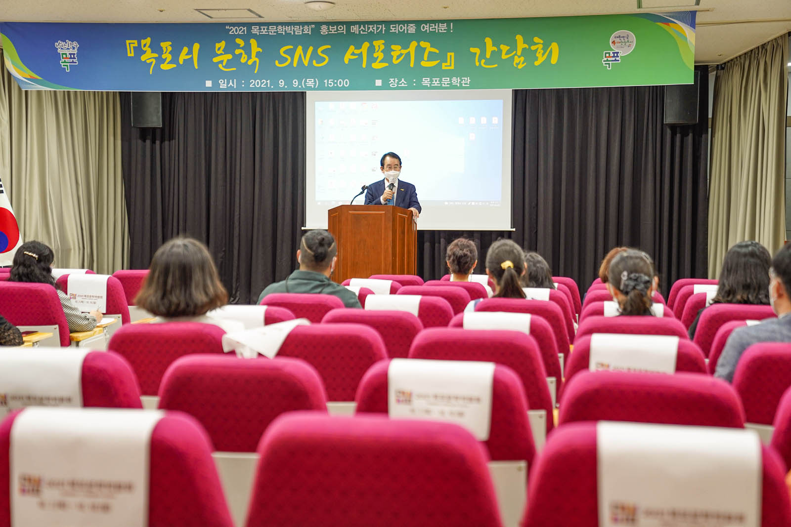 2021 목포문학박람회 홍보의 메신저가 되어줄 여러분! [목포시 문학 SNS 서포터즈] 간담회 일시:2021.9.9(목) 15:00 장소:목포문학관 이라고 쓰여진 현수막이 걸린 강당에서 시장님이 기념사를 하고 있다. 