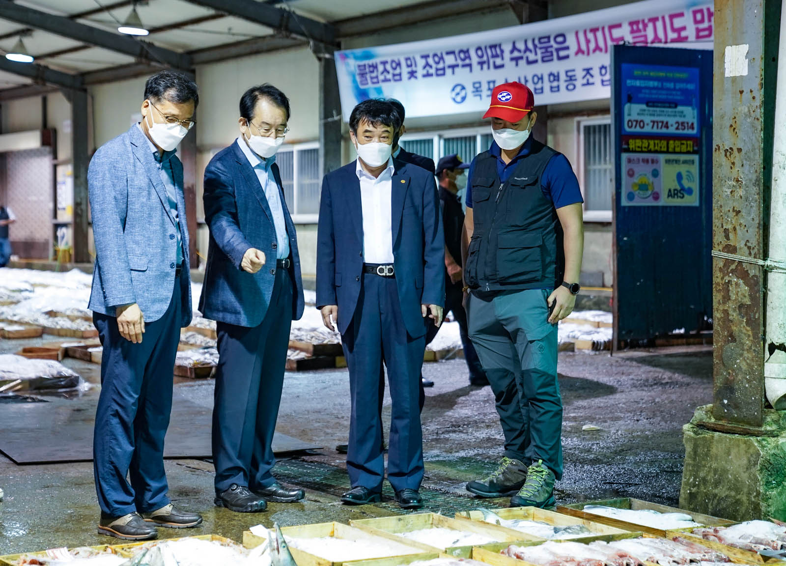 수협위판장에서 수산물을 바라보며 이야기 나누고 있는 사진이다. 앞뒤로 바닥에 수산물 좌판이 즐비해 있다.