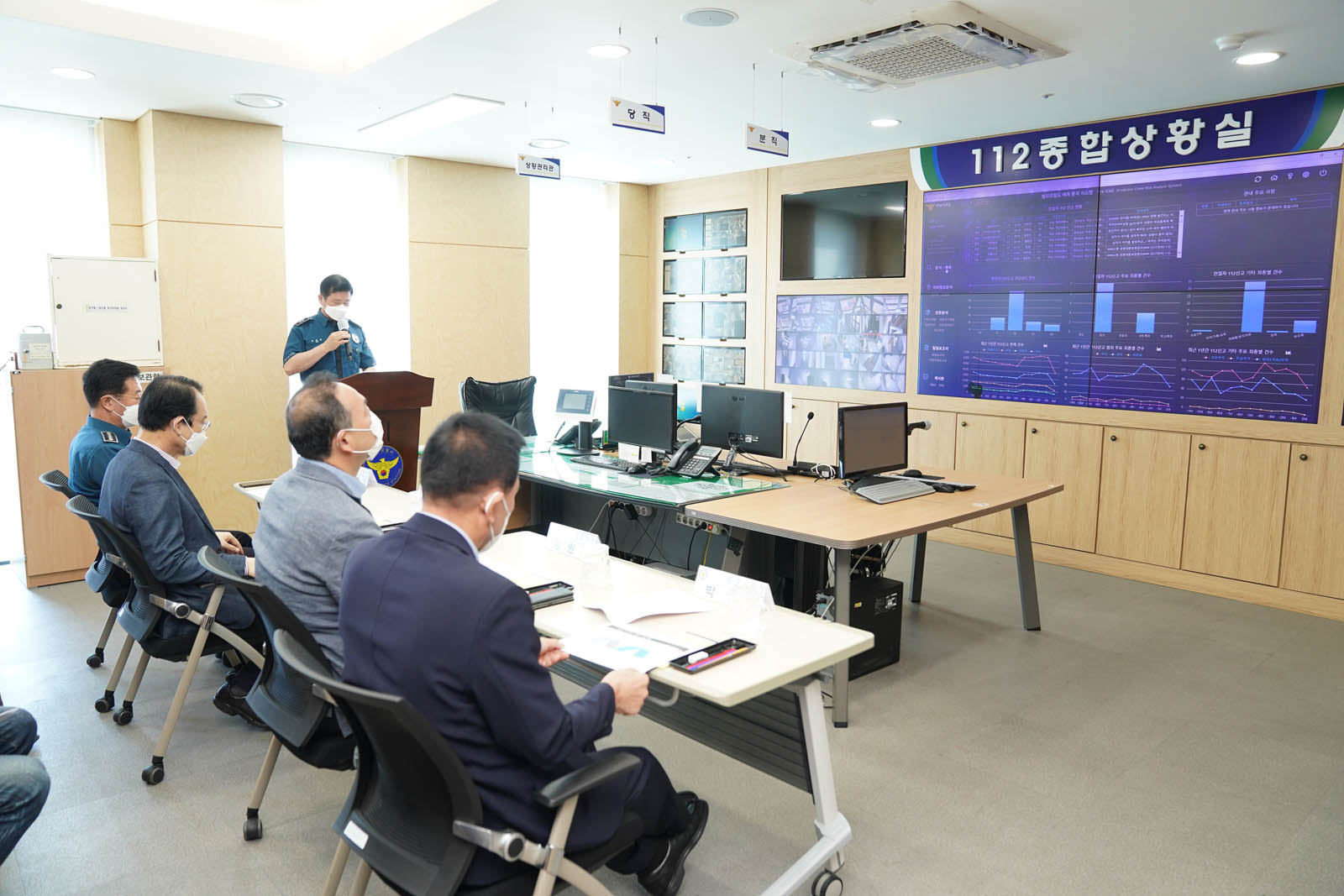 시장님과 관계자들이 112 종합 상황실에서 스크린에 자료를 보며 설명 듣고 있는 사진