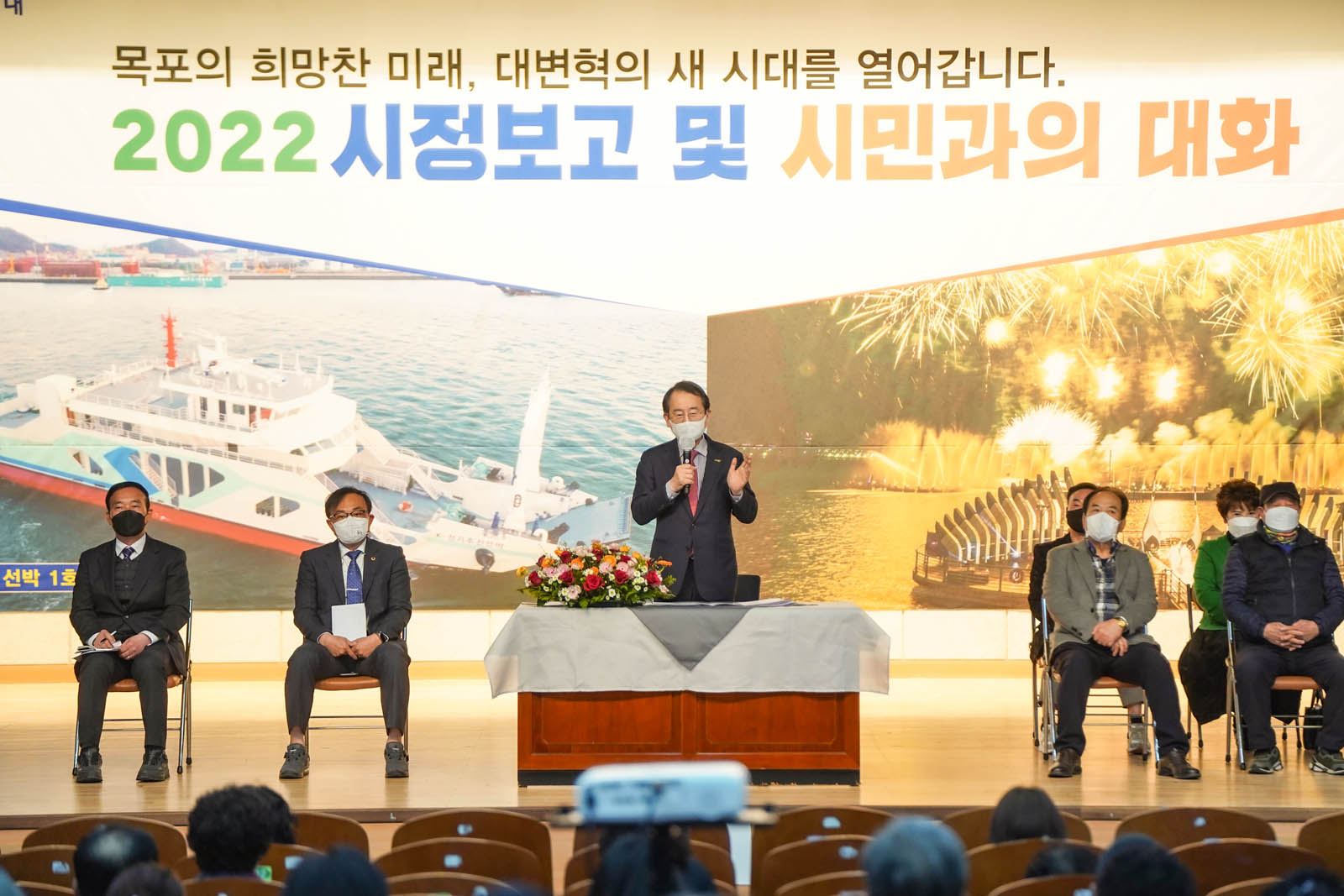 (03.22.해양수산복합센터)  시정보고 및 시민과의 대화에서 목포시장이 연설하고 있고 양쪽에 관계자들이 의자에 착석해 있다.