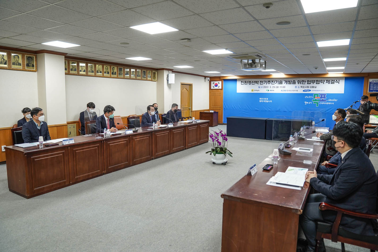 (03.29.상황실) 업무협약 체결식을 진행중인 모습으로 참석자들이 양 쪽으로 테이블을 놓고 마주보며 앉아 있다