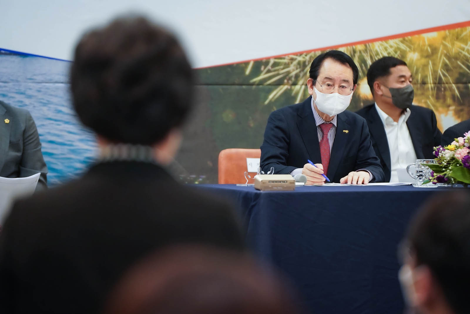 (03.30.에메랄드웨딩홀) 한 시민이 일어서서 이야기하고 있고 목포 시장이 손에 펜을 듣고 진지하게 이야기를 듣고 있다.