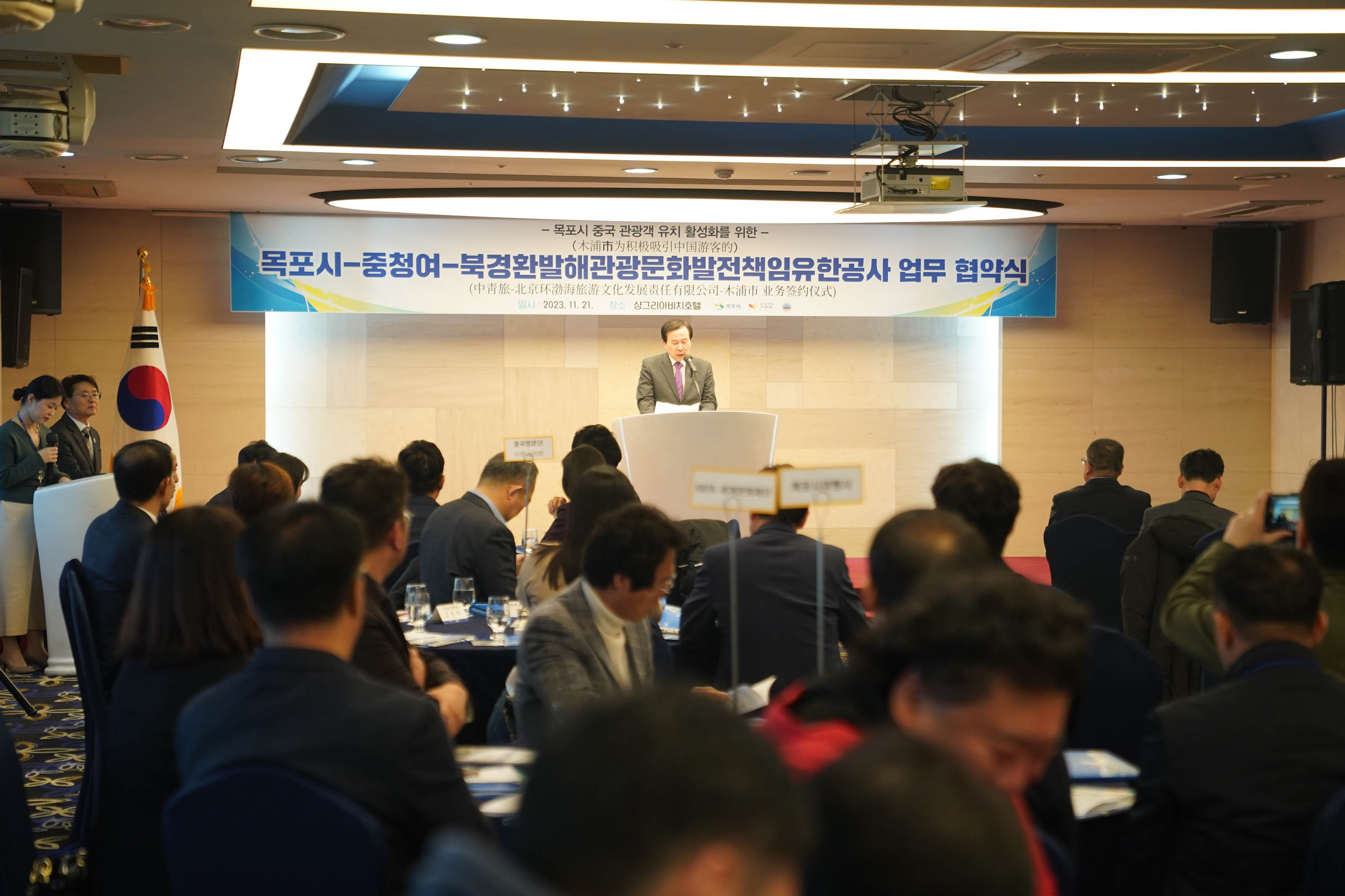 목포시 중청여 북경환발해관광문화발전책임유한공사 업무 협약식 플랜카드를 뒤에두고 단상위에서 박홍률 목포시장이 연설하는 모습과 경청하는 관계자들