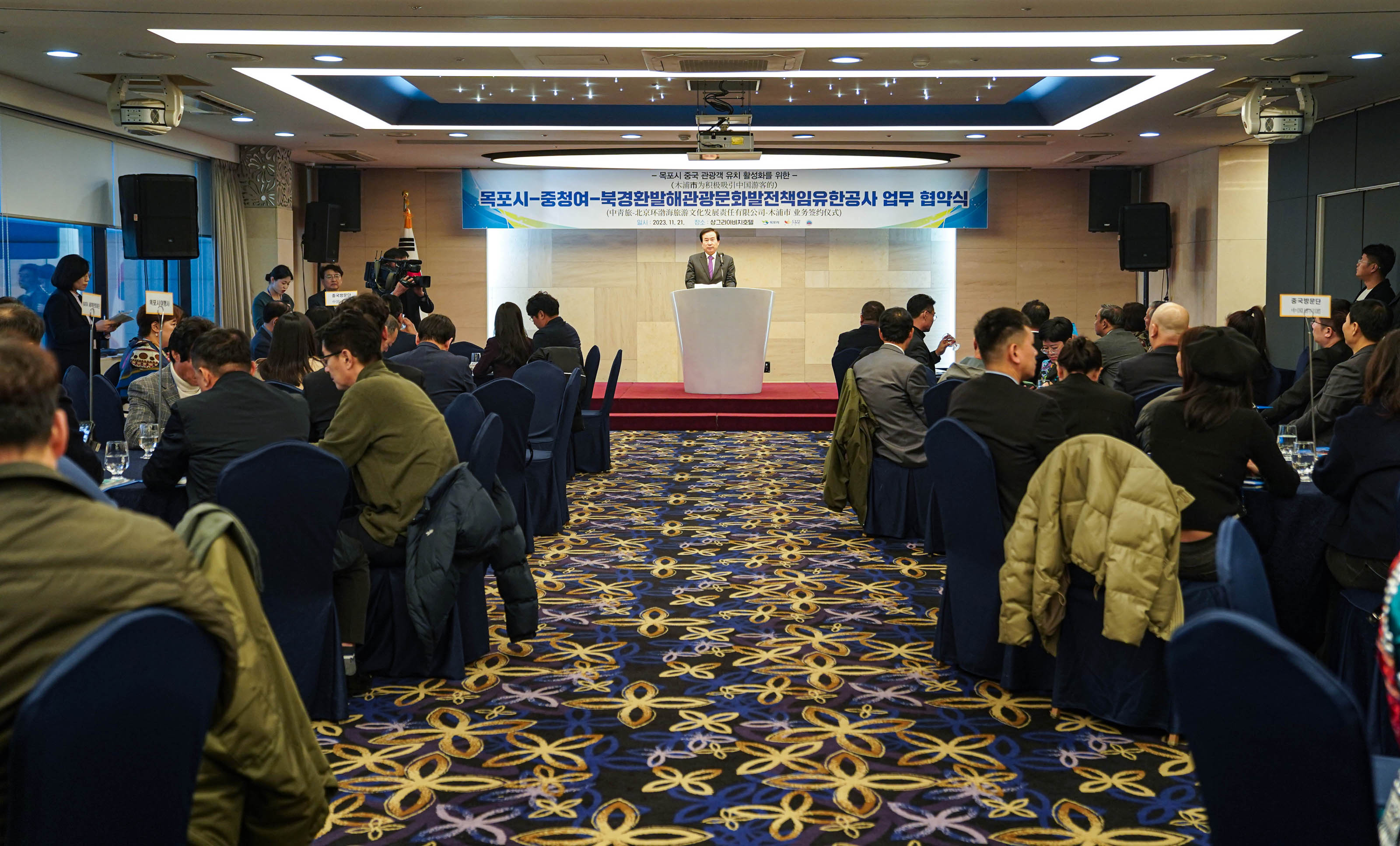 목포시 중청여 북경환발해관광문화발전책임유한공사 업무 협약식 플랜카드를 뒤에두고 단상위에서 박홍률 목포시장이 연설하는 모습과 경청하는 관계자들
