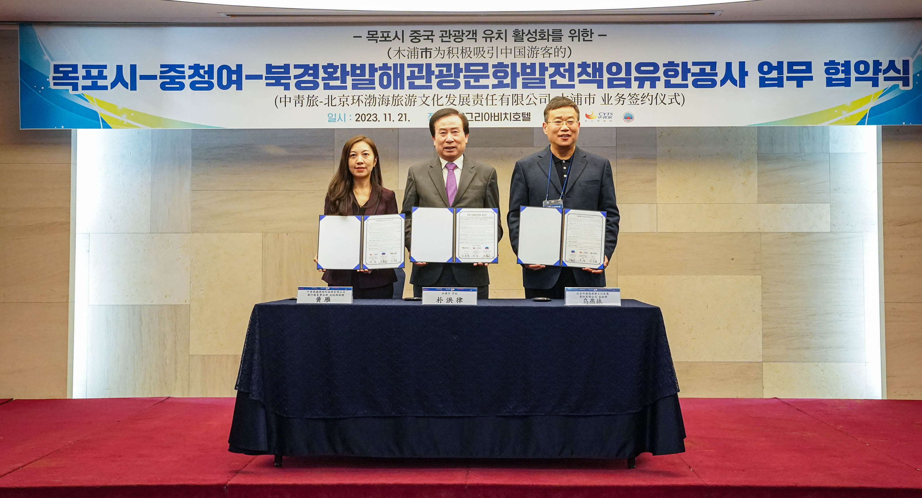 목포시 중국 관광객 유치 활성화를 위한 목포시 중청여 북경환발해관광문화발전책임유한공사 업무 협약식 플랜카드를 뒤에두고 단상위에서 협약관련 문서를 들고있는 관계자 두명과 박홍률 목포시장