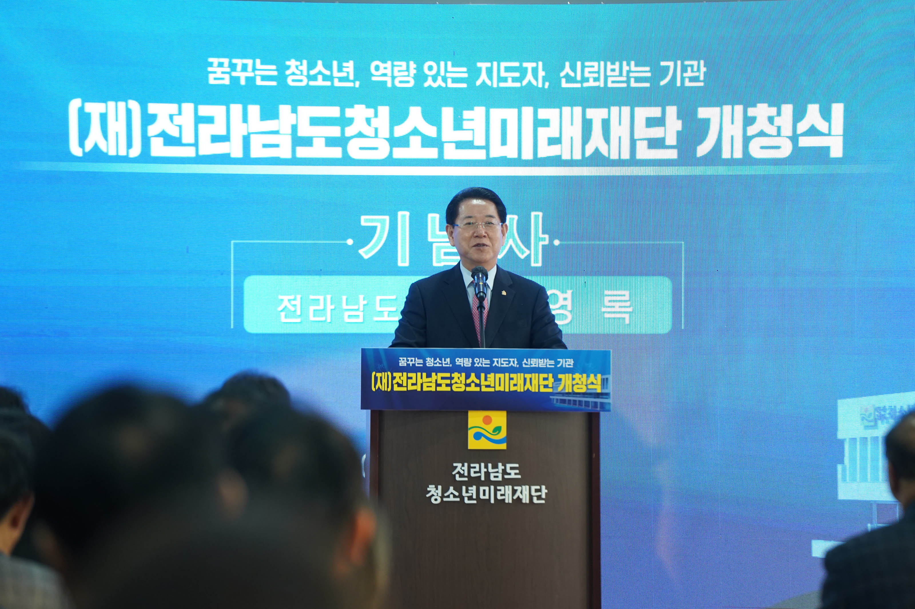 꿈꾸는 청소년, 역량 있는 지도자, 신뢰받는 기관 (재)전라남도 청소년미래재단 개청식 글을 배경으로두고 전라남도 청소년미래재단 단상에서 연설하는 도지사 김영록