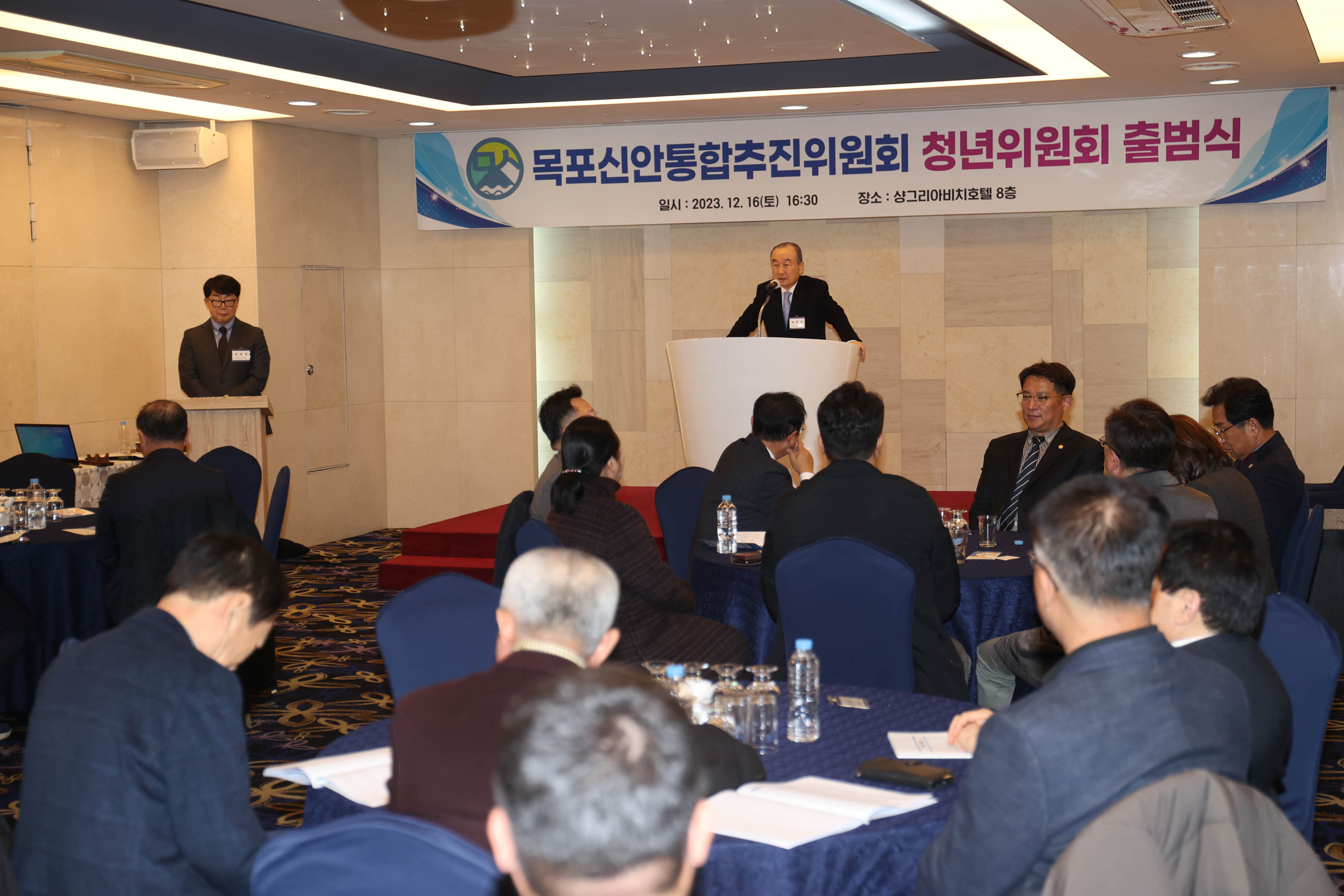 목포신안통합추진위원회 청년위원회 출범식 플랜카드가 걸린 연단위에서 연설하는 관계자와 경청하는 청중들