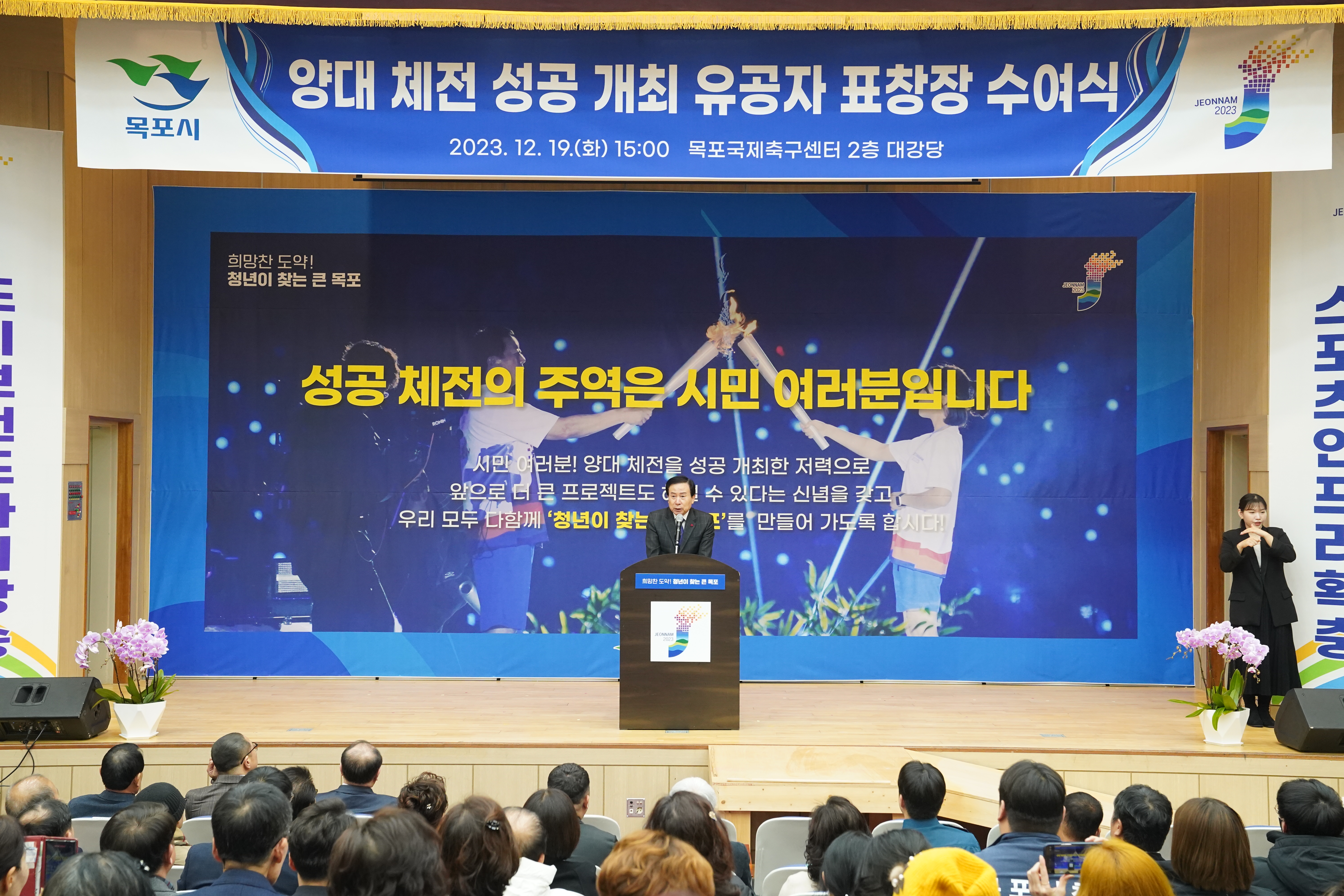 성공 체전의 주역은 시민여러분입니다. 글이 적힌 배경을 두고 연설하는 목포시장 박홍률과 경청하는 청중