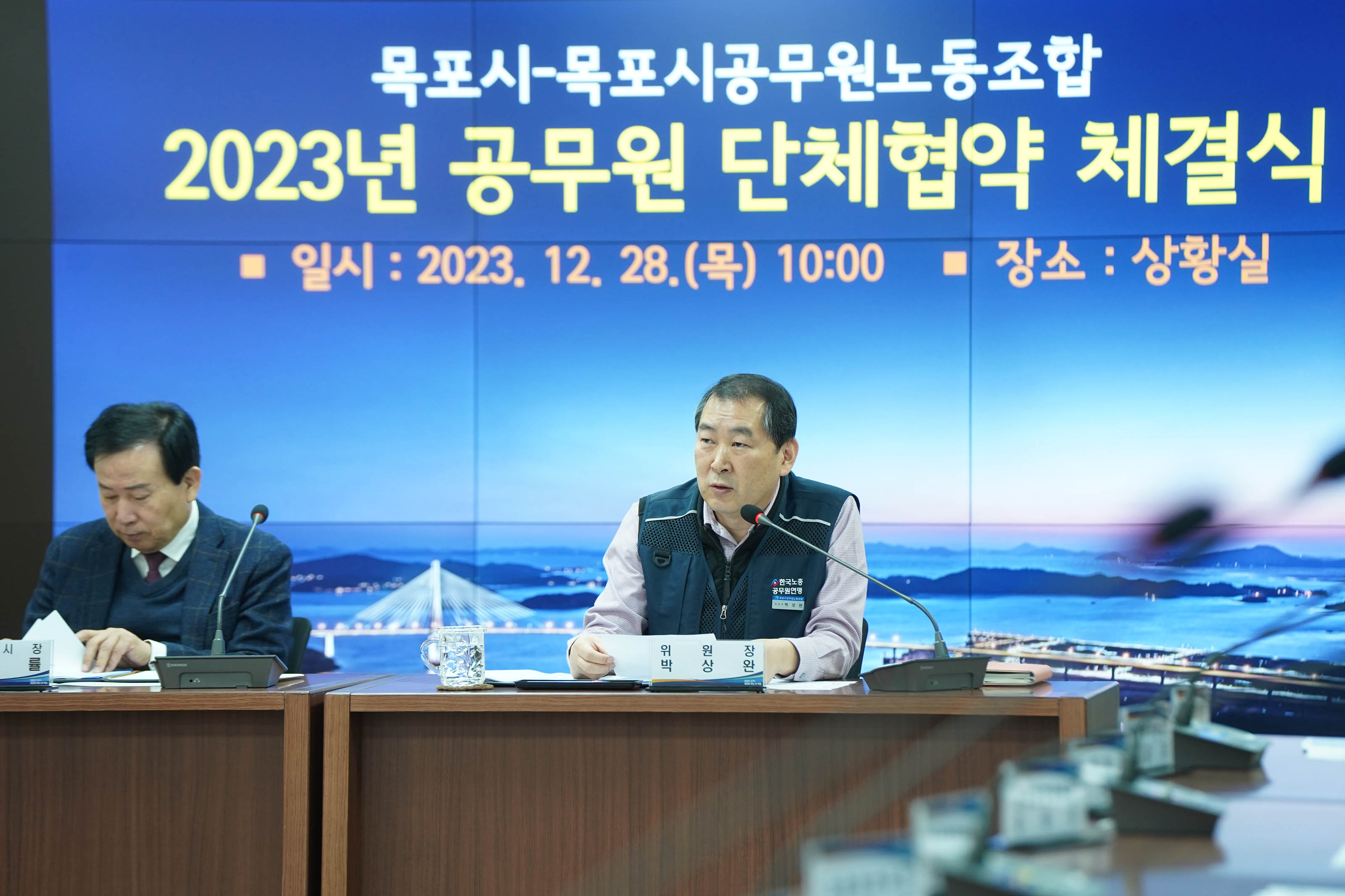 목포시 목포시공무원노동조합 2023 공무원 단체협약 체결식 일시 : 2023.12.28(목) 10:00 장소:상황실이 적혀있는 배경 앞에서 첨언중인 위원장과 경청하는 목포시장 박홍률