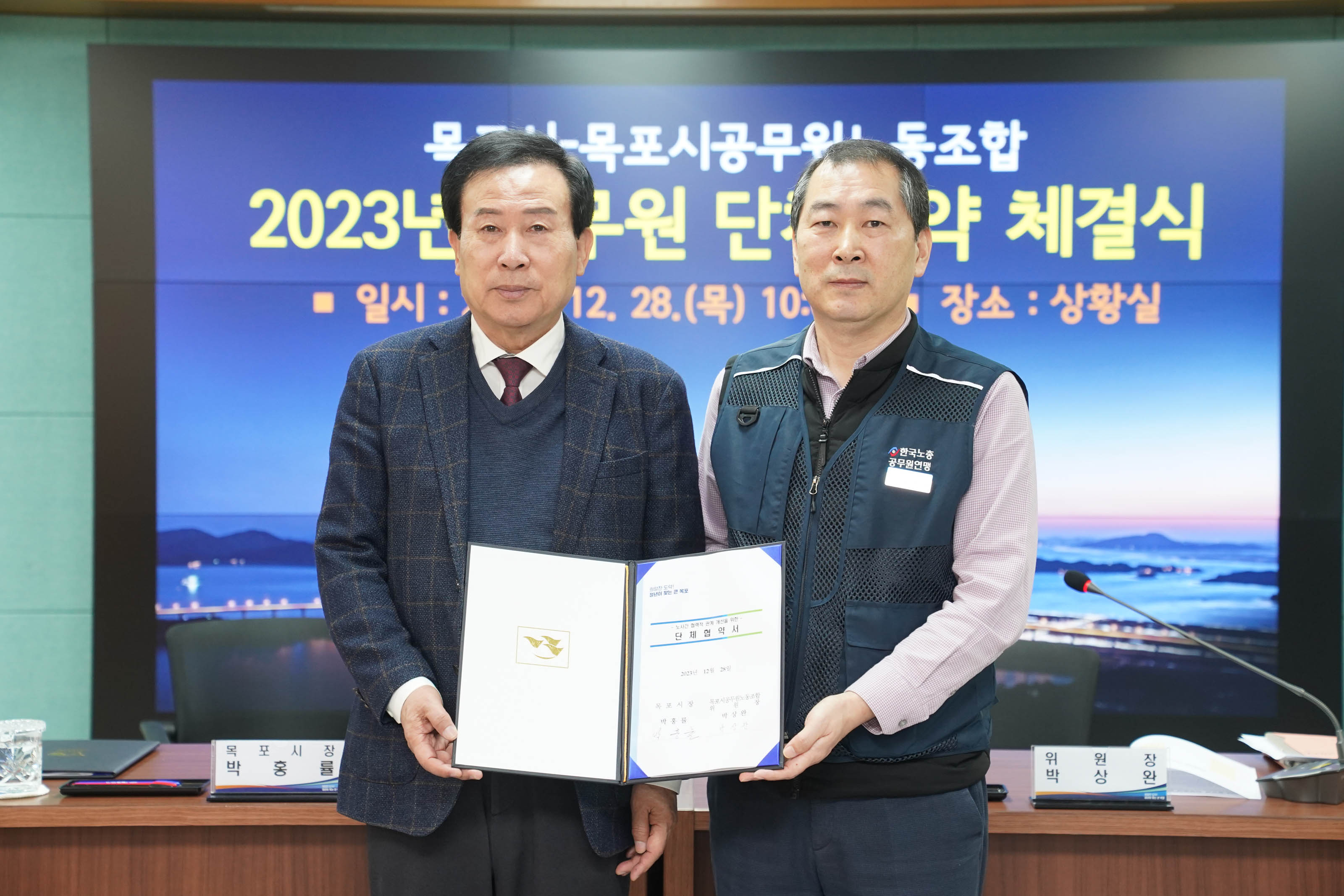 목포시 목포시공무원노동조합 2023 공무원 단체협약 체결식 일시 : 2023.12.28(목) 10:00 장소:상황실이 적혀있는 배경 앞에서 협력서를 들고있는 박홍률 목포시장과 위원장