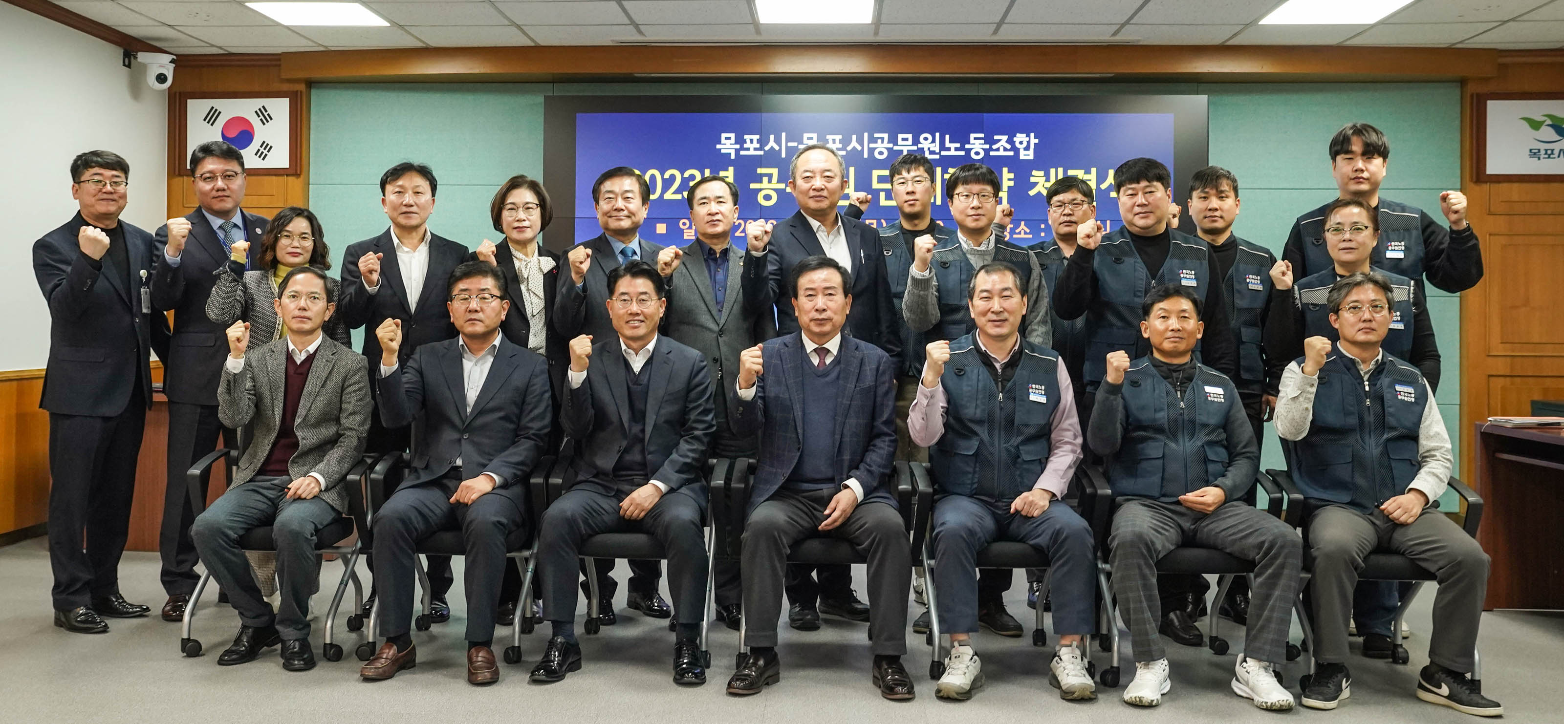 목포시 목포시공무원노동조합 2023 공무원 단체협약 체결식 일시 : 2023.12.28(목) 10:00 장소:상황실이 적혀있는 배경 앞에서 화이팅 포즈를 취하며 단체사진찍는 관계자들