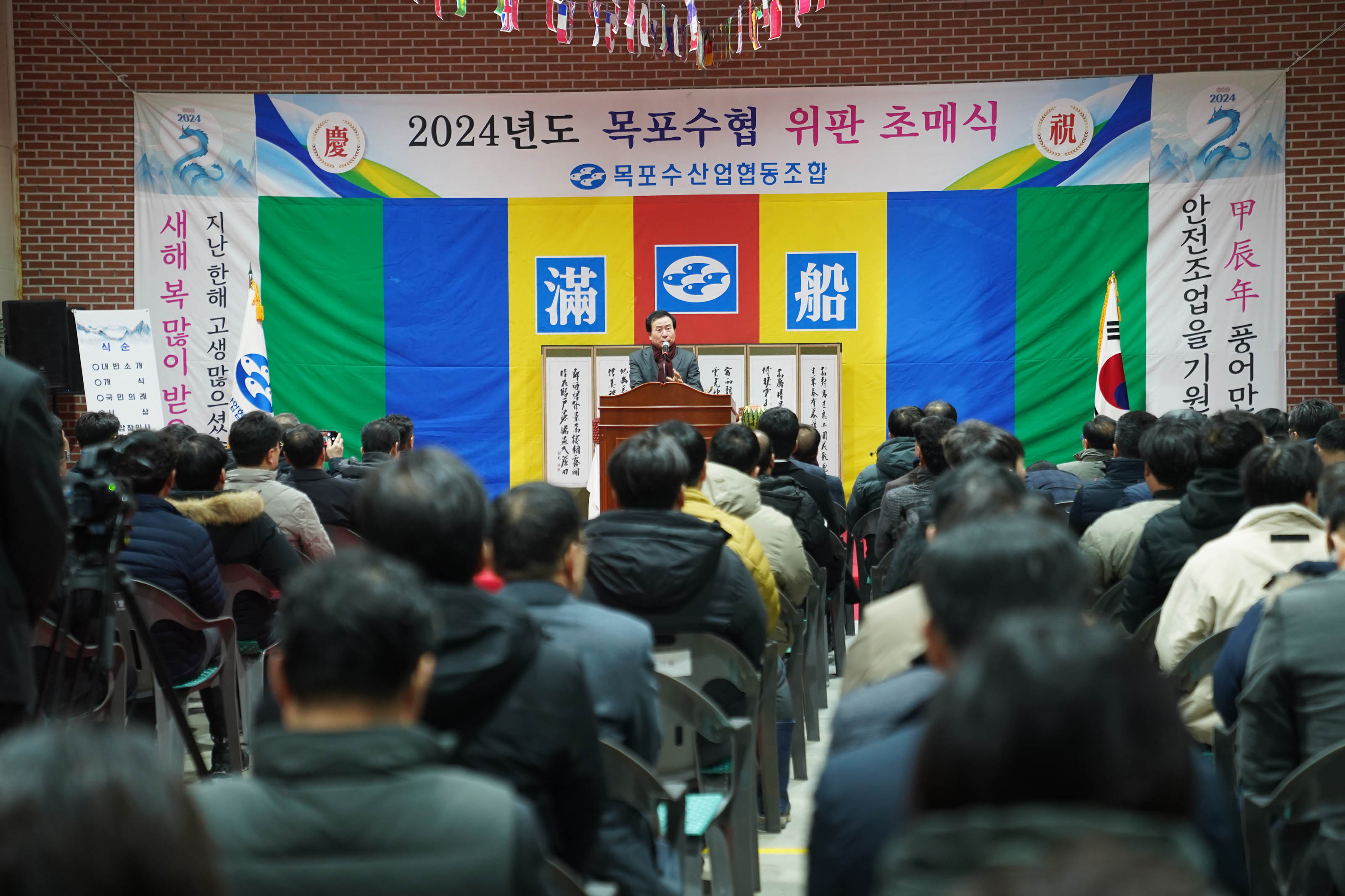 2024년도 목포수협 위판 초매식 목포수산업협동조합 현수막과 지난해 고생많으셨습니다 새해복많이 받으세요 현수막을 배경으로 두고 연단에서 연설중인 시장 박홍률과 경청하는 청중