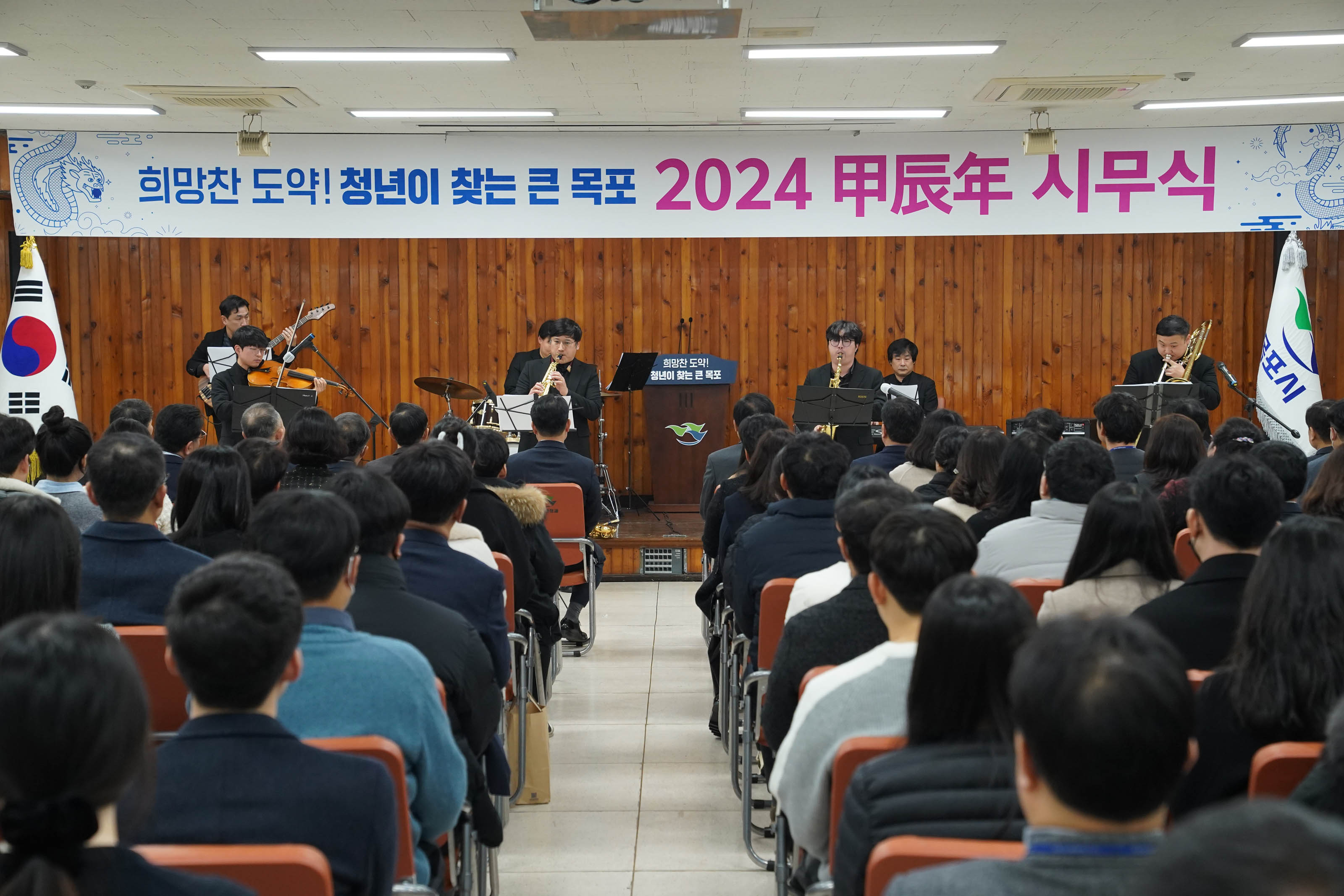 희망찬 도약! 청년이 찾는 큰 목포 2024 甲辰年 시무식 현수막이 걸린 무대위에서 연주중인 사람들과 경청하는 청중들 정면사진