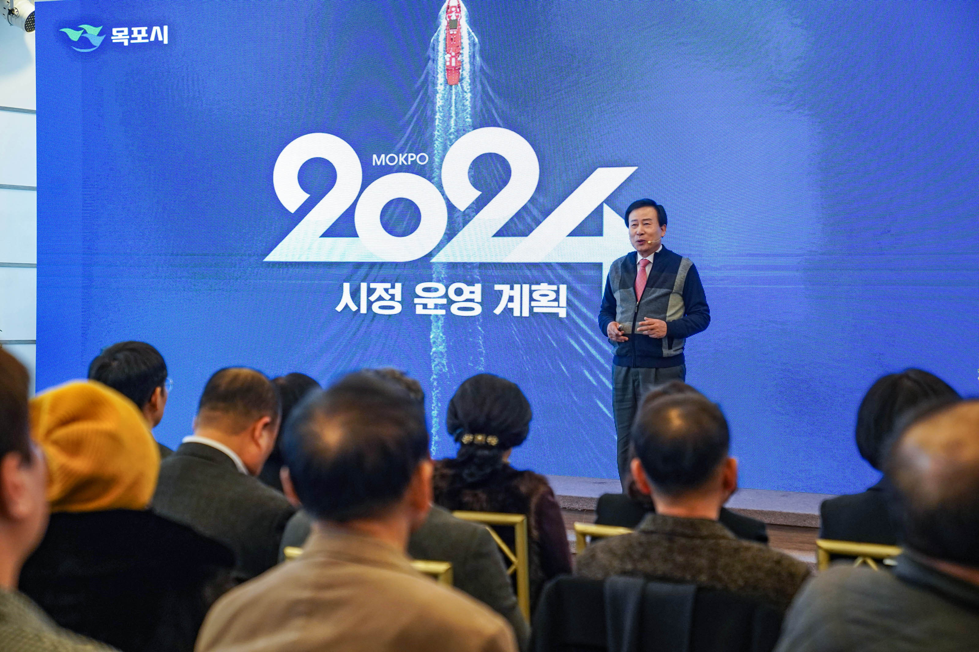 목포시 MOKPO2024 시정운영계획 글을 배경으로 두고 시민들과 소통중인 박홍률 시장과 경청중인 시민들