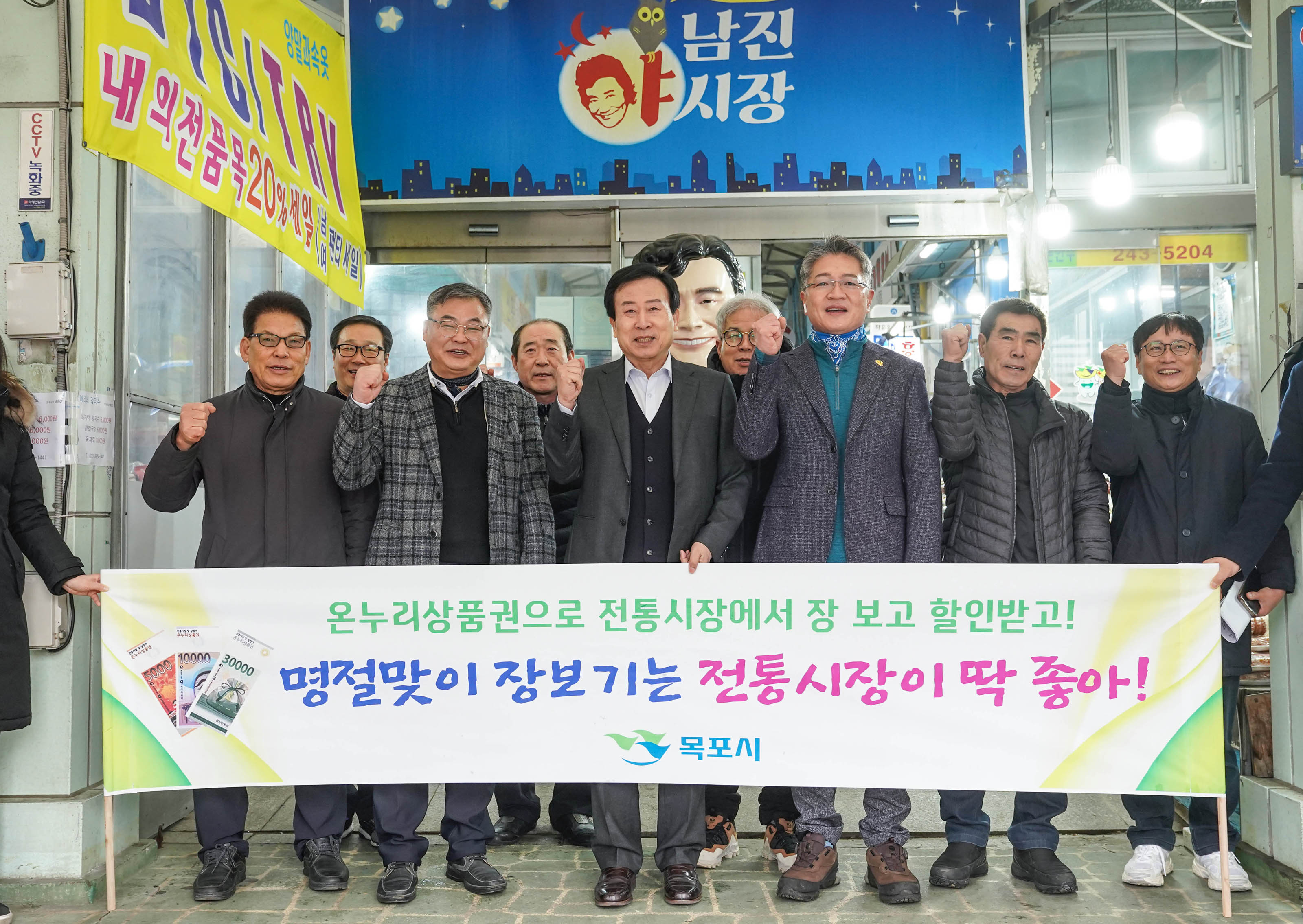 남진야시장 배경으로 온누리상품권으로 전통시장에서 장 보고 할인받고! 명절맞이 장보기는 전통시장이 딱 좋아! 목포시장 플랜카드를 들고 화이팅 포즈를 취하는 박홍률 시장과 관계자들