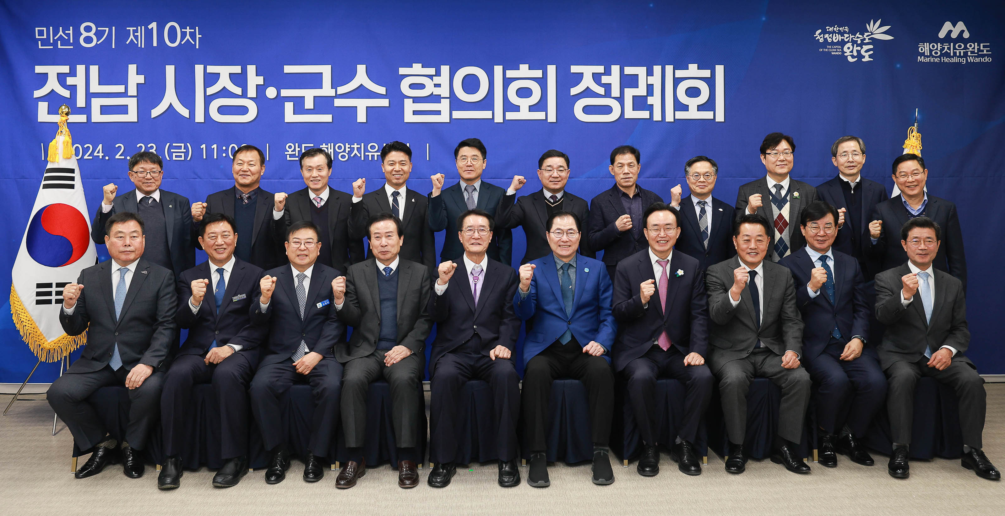 민선 8기 제10차 전남 시장·군수 협의회 정례회 2024.2.23(금) 11:00 | 완도 해양치유센터 | 현수막이 걸린 벽 앞에서 오른손으로 화이팅을 외치며 찍은 박홍률 시장을 포함한 21명의 단체 사진