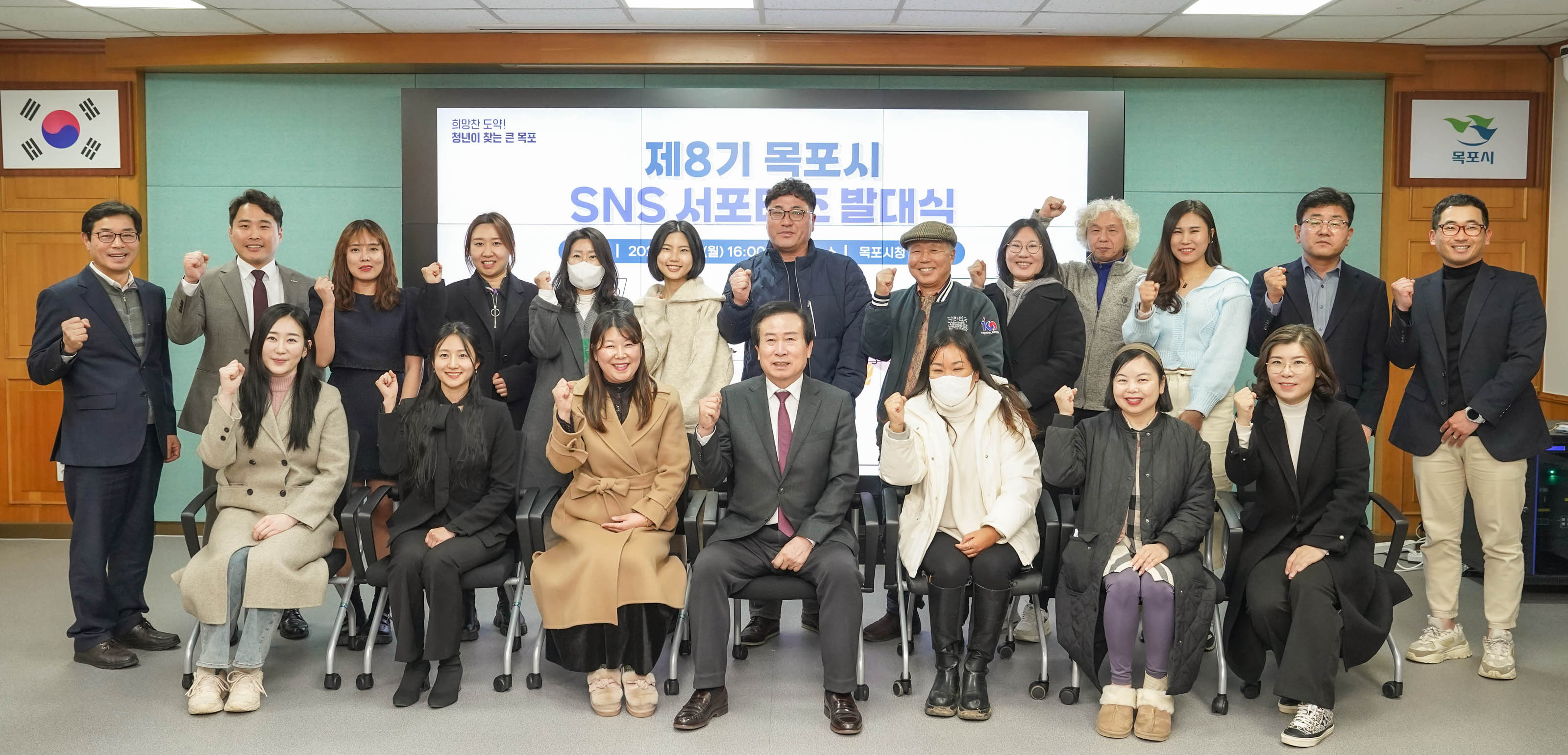 제8기 목포시 SNS 서포터즈 발대식이라는 화면 앞에서 박홍률 시장을 중심으로 다같이 화이팅을 하며 찍은, 박홍률 시장을 포함한 20명의 사람들