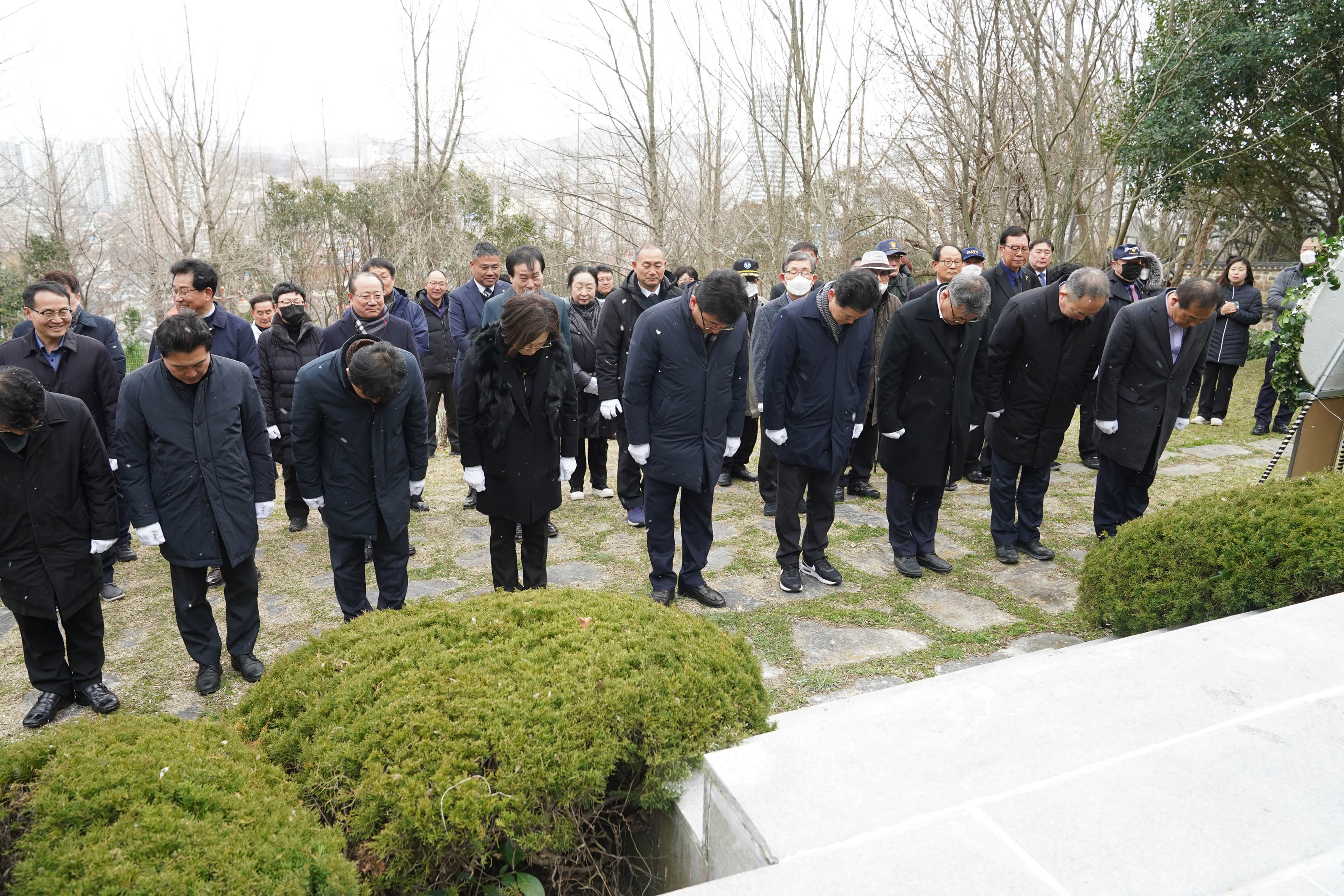 기념탑 아래에서 다 같이 묵념을 하고 있다. 30명 이상의 사람들이 서있다.