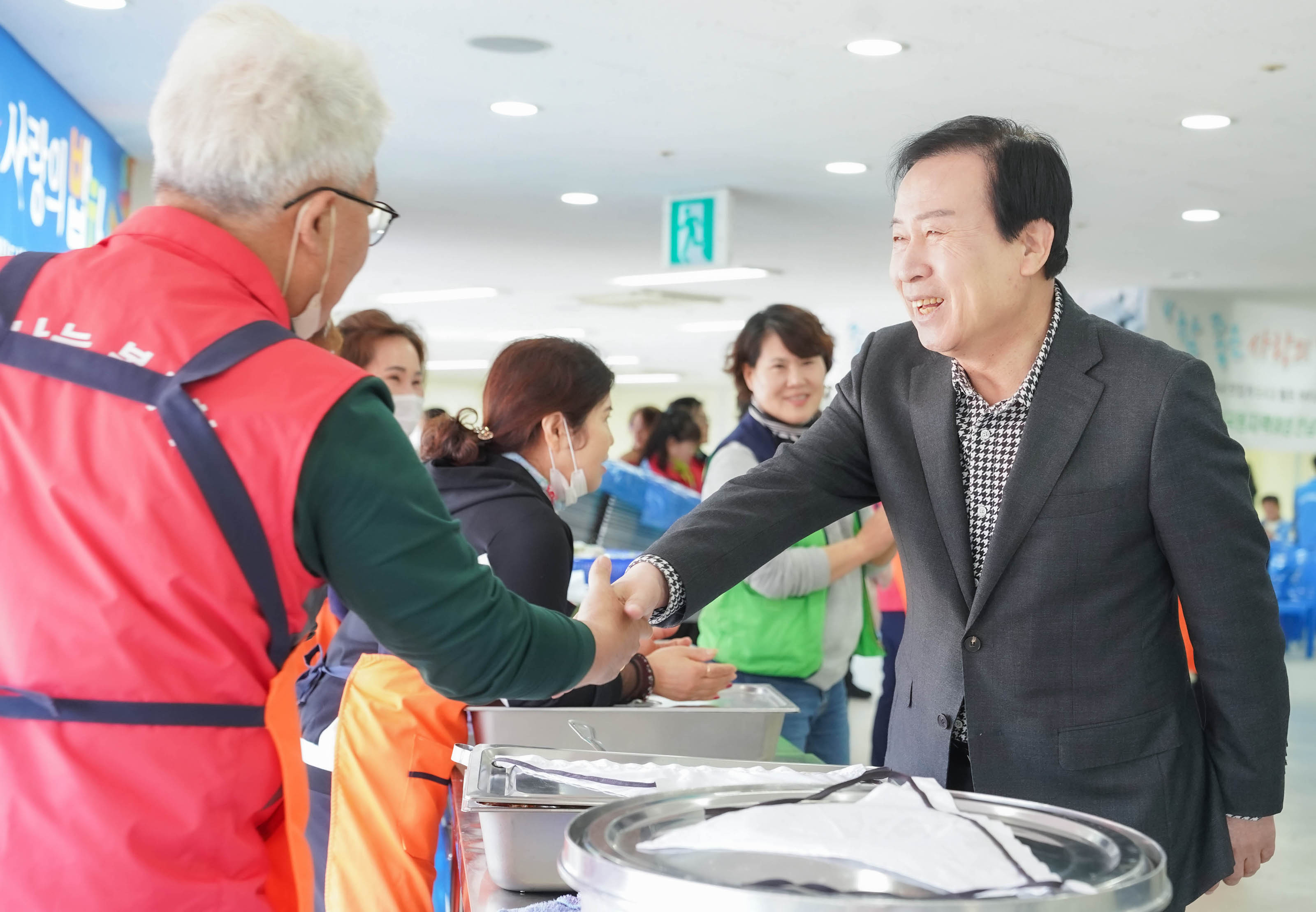 밥차 봉사를 하는 빨간 조끼 유니폼을 입은 남성과 악수하며 인사를 나누는 박홍률 시장의 사진