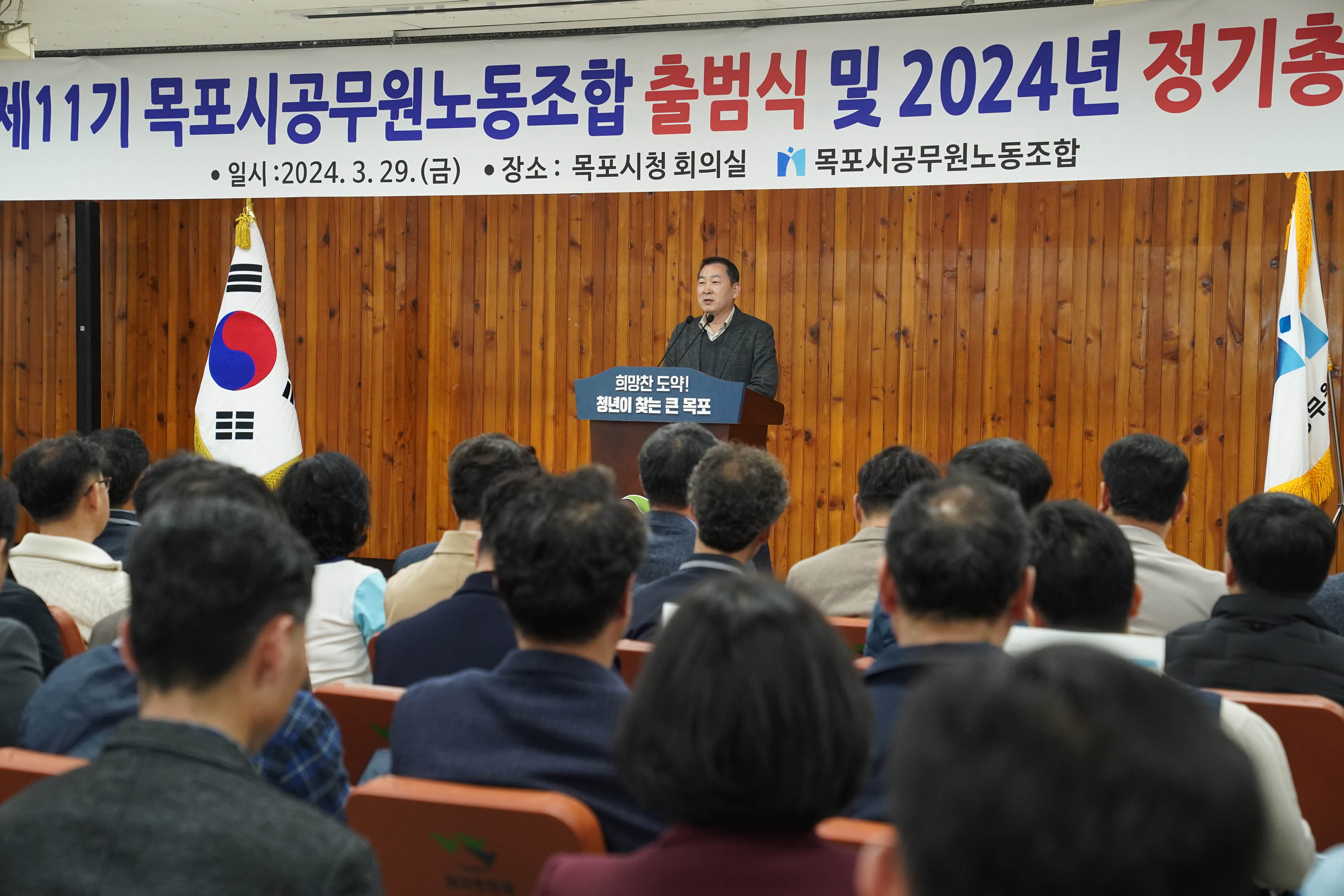 노동 조합 깃발을 흔들었던 남성이 희망찬 도약! 청년이 찾는 큰 목포 문구가 적힌 단상에 서서 얘기하고 있다.