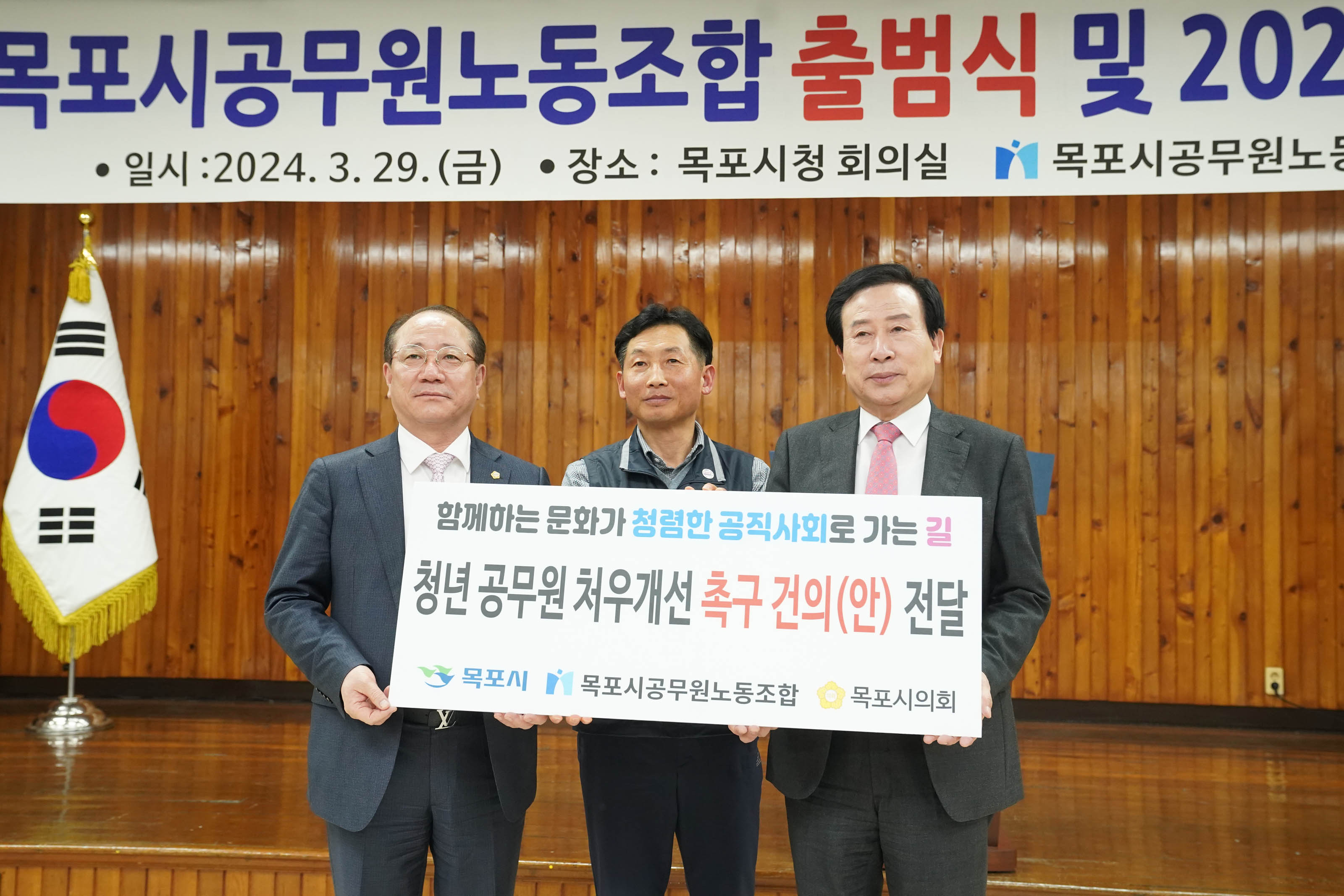 의회 뱃지를 달고 있는 듯한 중년의 남성과 노동 조합 조끼를 입은 중년 남성과 박홍률 시장 순으로 함께하는 문화가 청렴한 공직사회로 가는길 청년 공무원 처우개선 촉구 건의(안) 전달 목포시 목포시공무원노동조합 목포시의회 문구가 적힌 팻말을 들고 찍은 사진