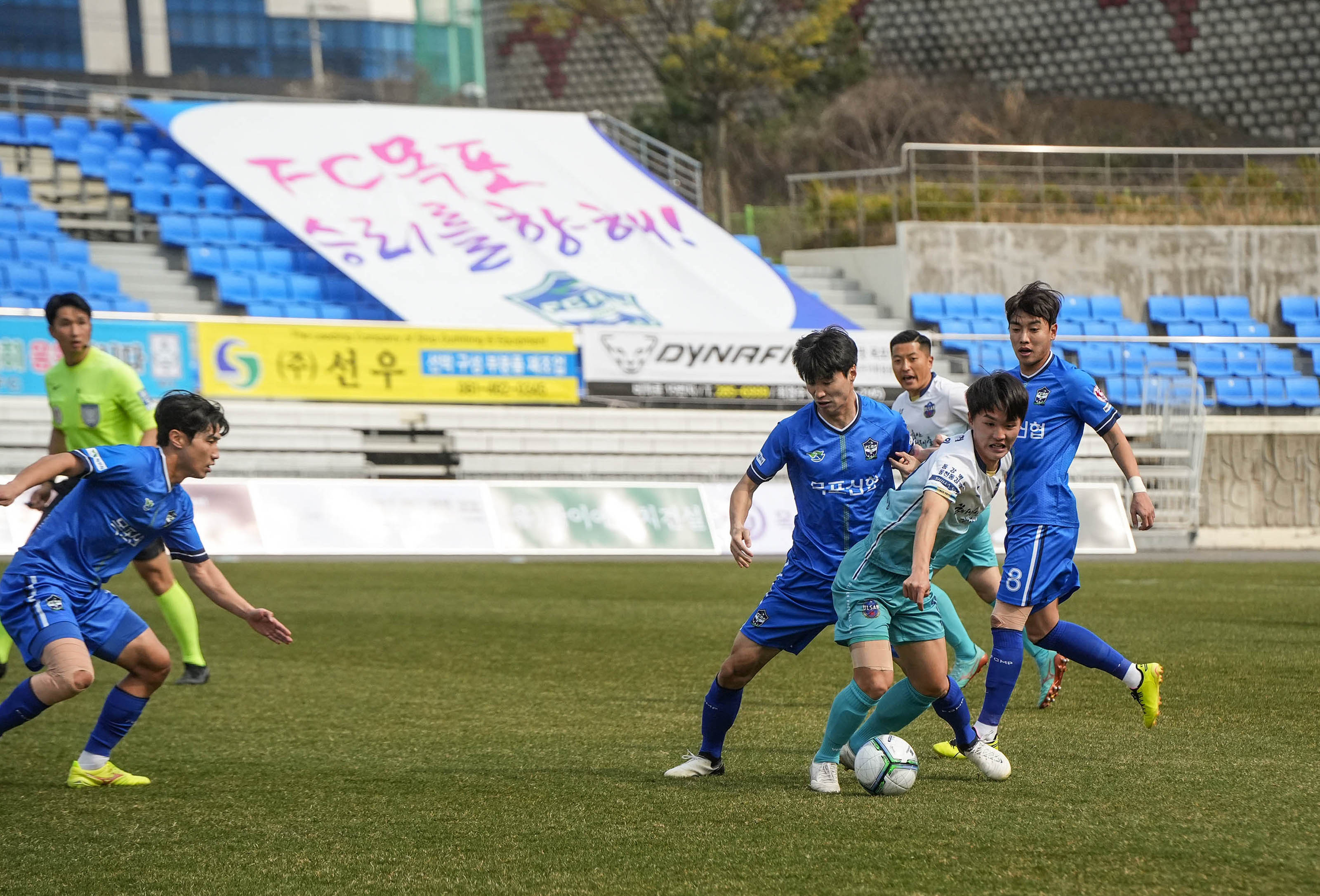 다섯명의 선수들이 뒤엉키며 축구 경기를 하는 사진. 뒤로 심판이 경기를 지켜보고 있다.