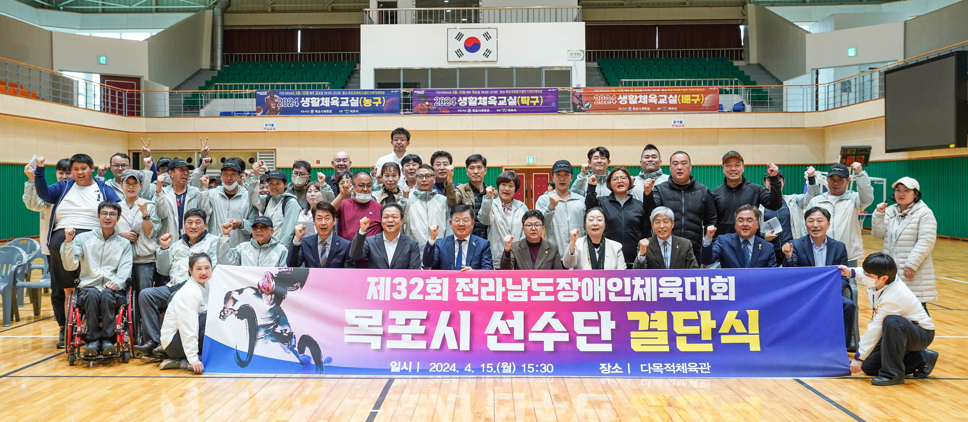 제32회 전라남도장애인체육대회 목포시 선수단 결단식 일시 2024.4.15(월) 15:30 장소 다목적체육관 현수막을 앞자리 사람들이 들고있고 참석자들이 다함께 화이팅 포즈를 하고있는 사진.