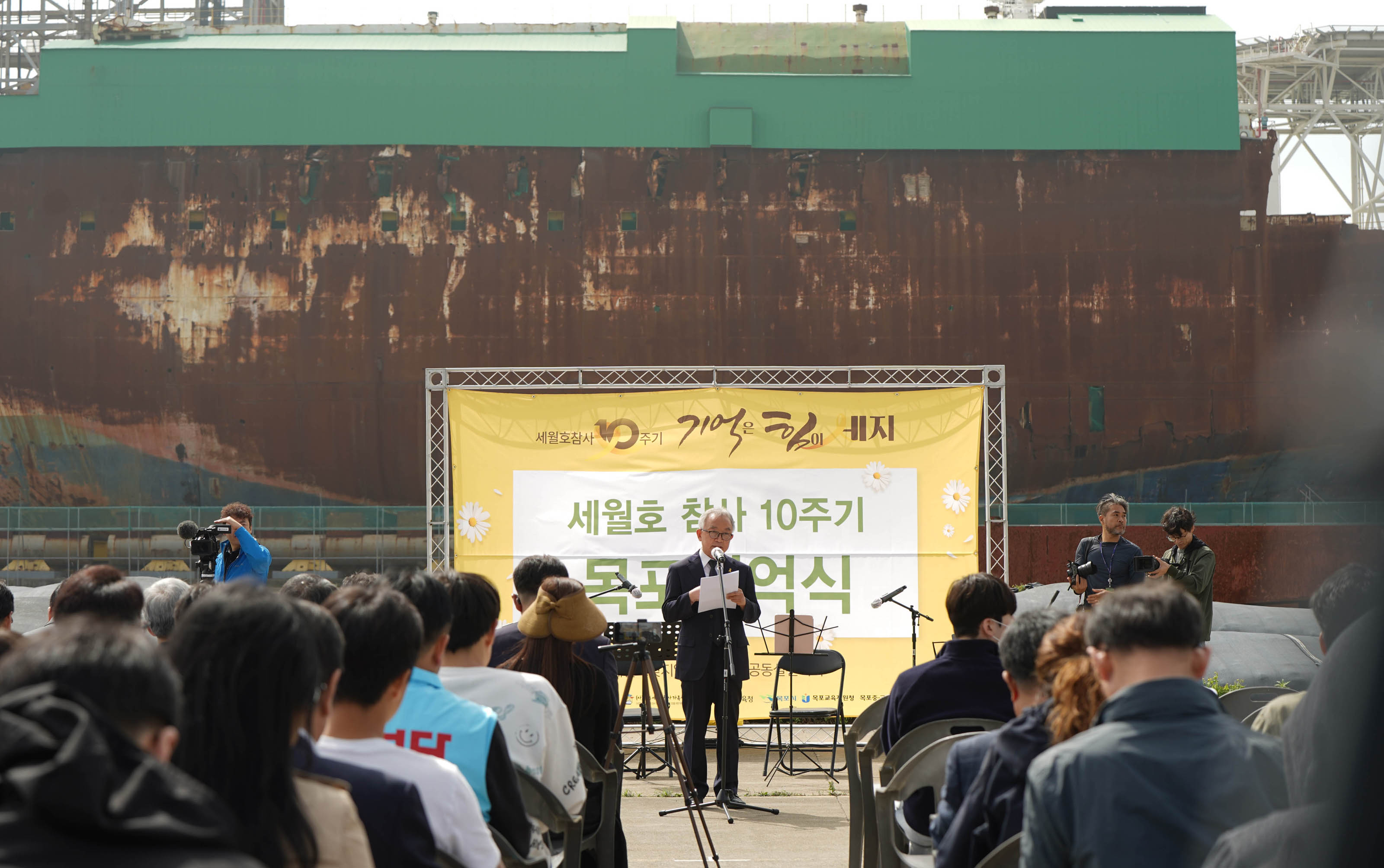 세월호 참사10주기 기억은 힘이 세지 세월호 참사 10주기 목포기억식 현수막을 배경으로 진행하고있는 사회자와 앉아서 경청하는 청중들