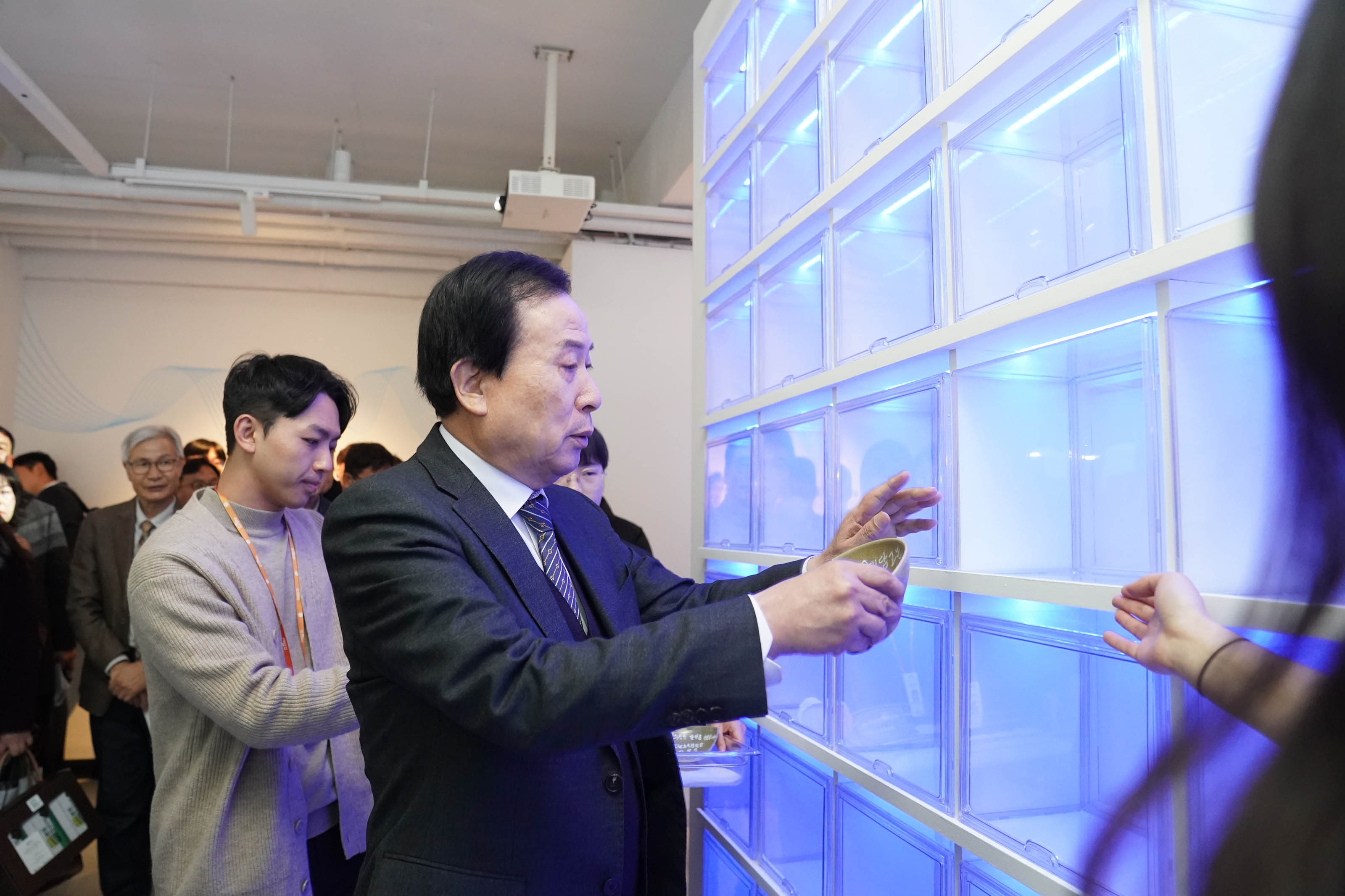 박홍률 목포시장이 체험을 마친 도자기 접시를 파란 조명이 켜진 전시 벽면 칸에 조심스럽게 넣고 있는 모습. 주위에는 관계자들과 시민들이 함께 지켜보고 있다.