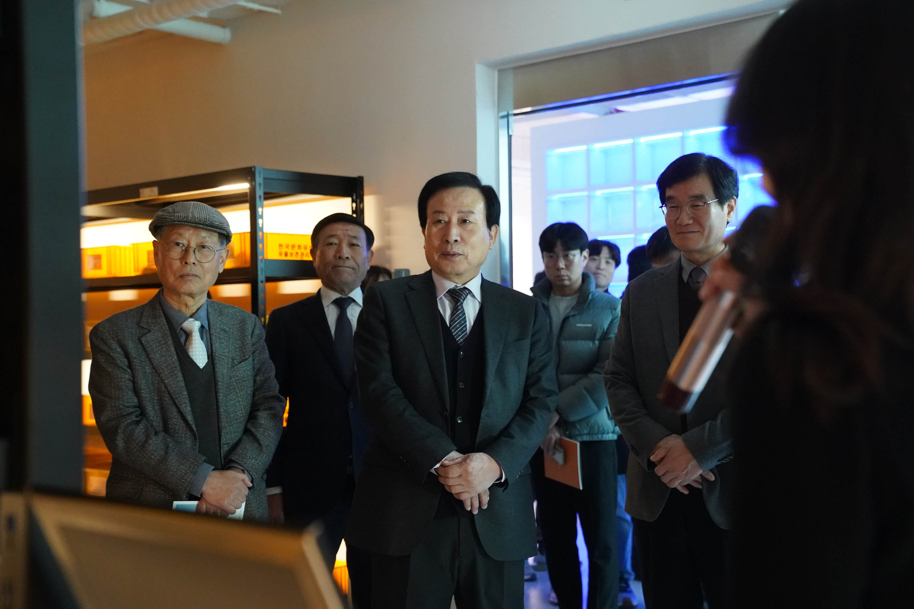 박홍률 목포시장과 관계자들이 조명이 어둡게 설정된 전시 공간에서 해설자의 설명을 진지하게 듣고 있는 모습. 배경에는 주황색 조명이 비친 진열장과 파란 조명의 체험 공간이 보이며, 참여자들은 손을 모으거나 설명에 집중한 표정을 짓고 있다.