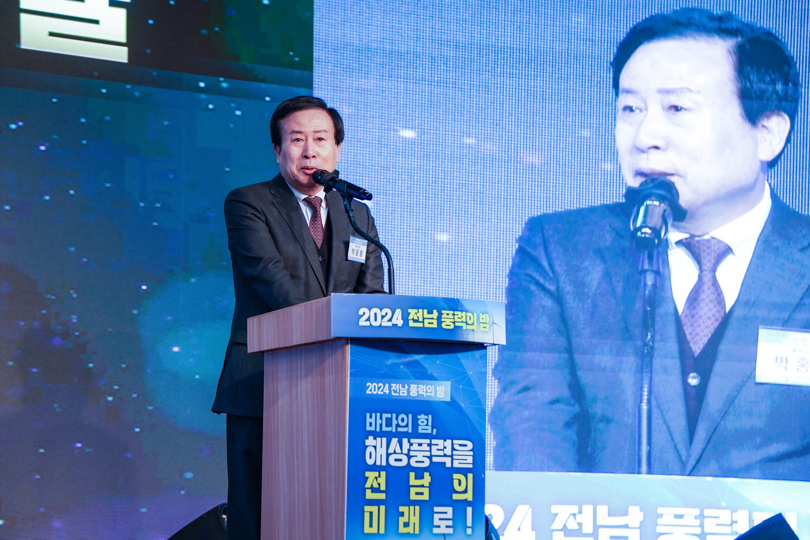 '2024 전남 풍력의 밤' 행사 무대에서 박홍률 목포시장이 단상에 서서 마이크를 통해 발언하고 있는 모습. 단상 전면에는 '2024 전남 풍력의 밤 바다의 힘, 해상풍력을 전남의 미래로!'라는 문구가 적혀 있고, 오른쪽 대형 스크린에는 연설자의 모습이 실시간으로 비춰지고 있다.