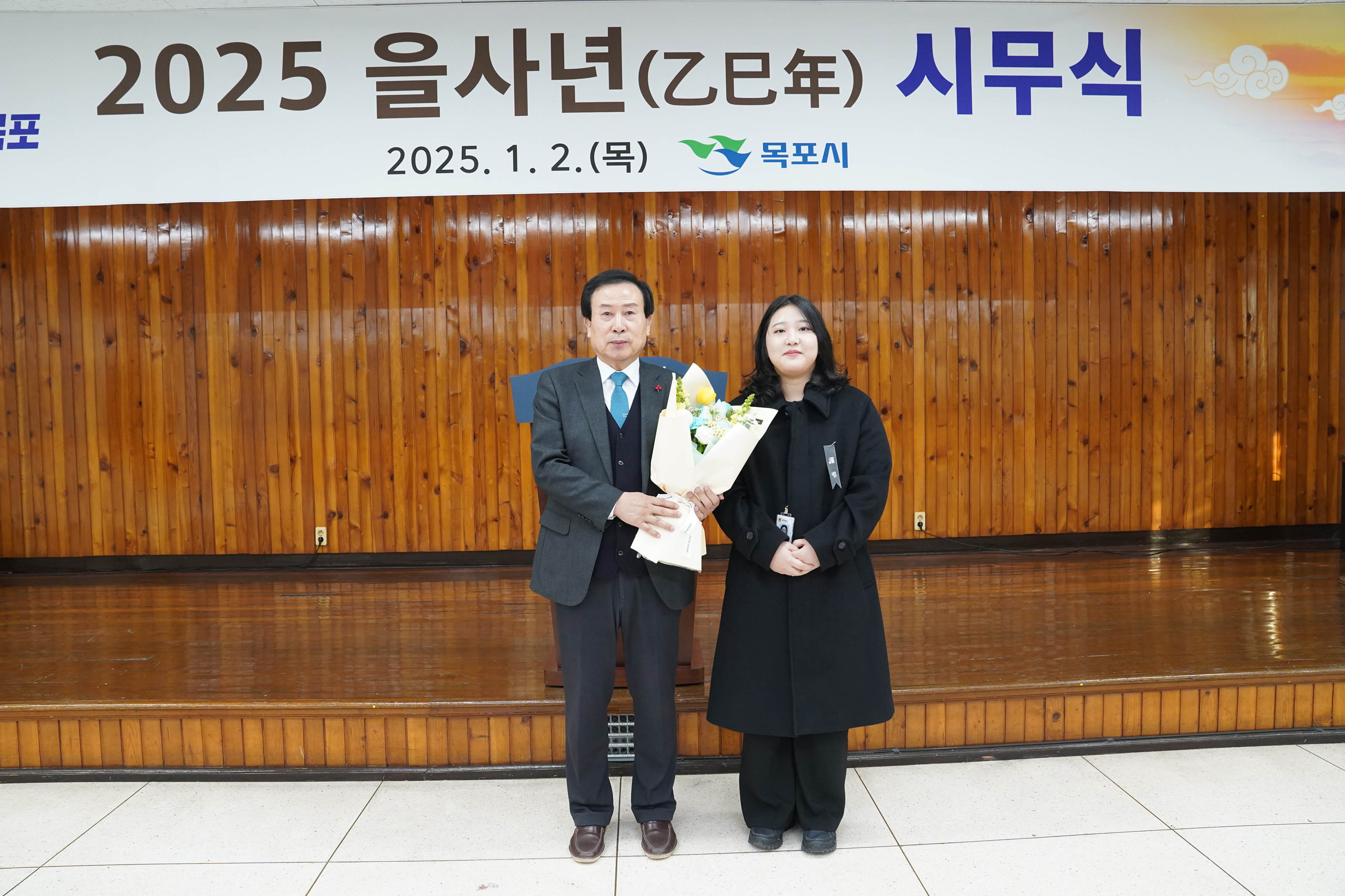 2025 을사년 시무식에서 박홍률 목포시장이 꽃다발을 들고 한 여성과 함께 기념사진을 찍고 있는 모습. 배경에는 '2025 을사년 시무식 2025.1.2 (목) 목포시'라는 문구가 적힌 현수막이 보인다.