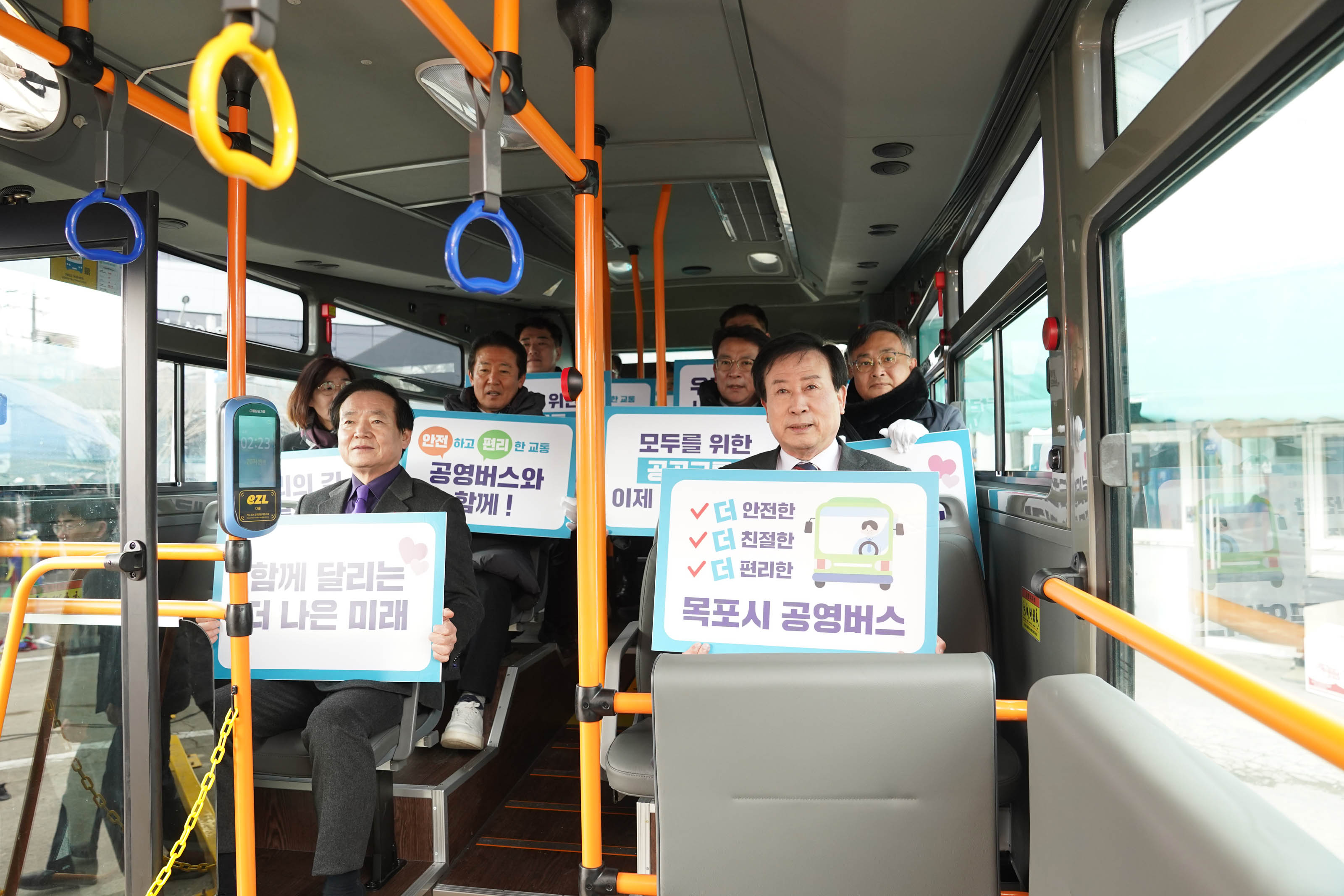 목포시 공영버스 출범식에 참석한 박홍률 목포시장을 비롯한 주요 인사들이 버스 안에서 공영버스와 관련된 표어가 적힌 팻말을 들고 있다. 표어에는 각각 '더 안전한 더 친절한 목포시 공영버스', '함께 달리는 더 나은 미래' 등이 적혀 있다.