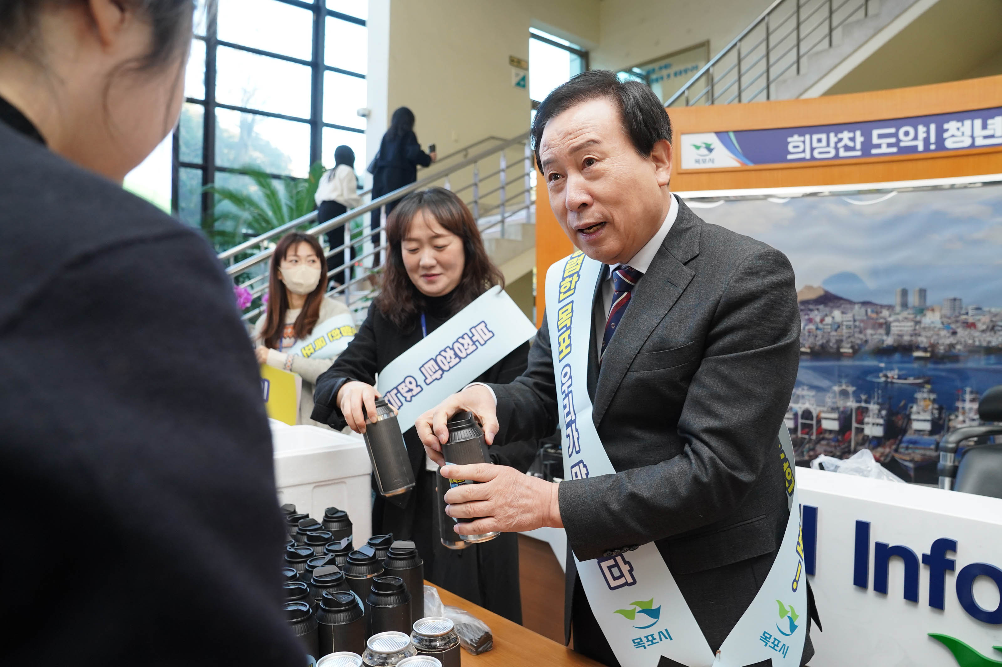 박홍률 목포시장이 청렴 캠페인에 참여한 시민들에게 텀블러를 나누어주며 대화하는 모습. 시장은 리본을 착용하고 시민들과 소통하고 있으며, 캠페인 물품들이 테이블에 놓여 있다.