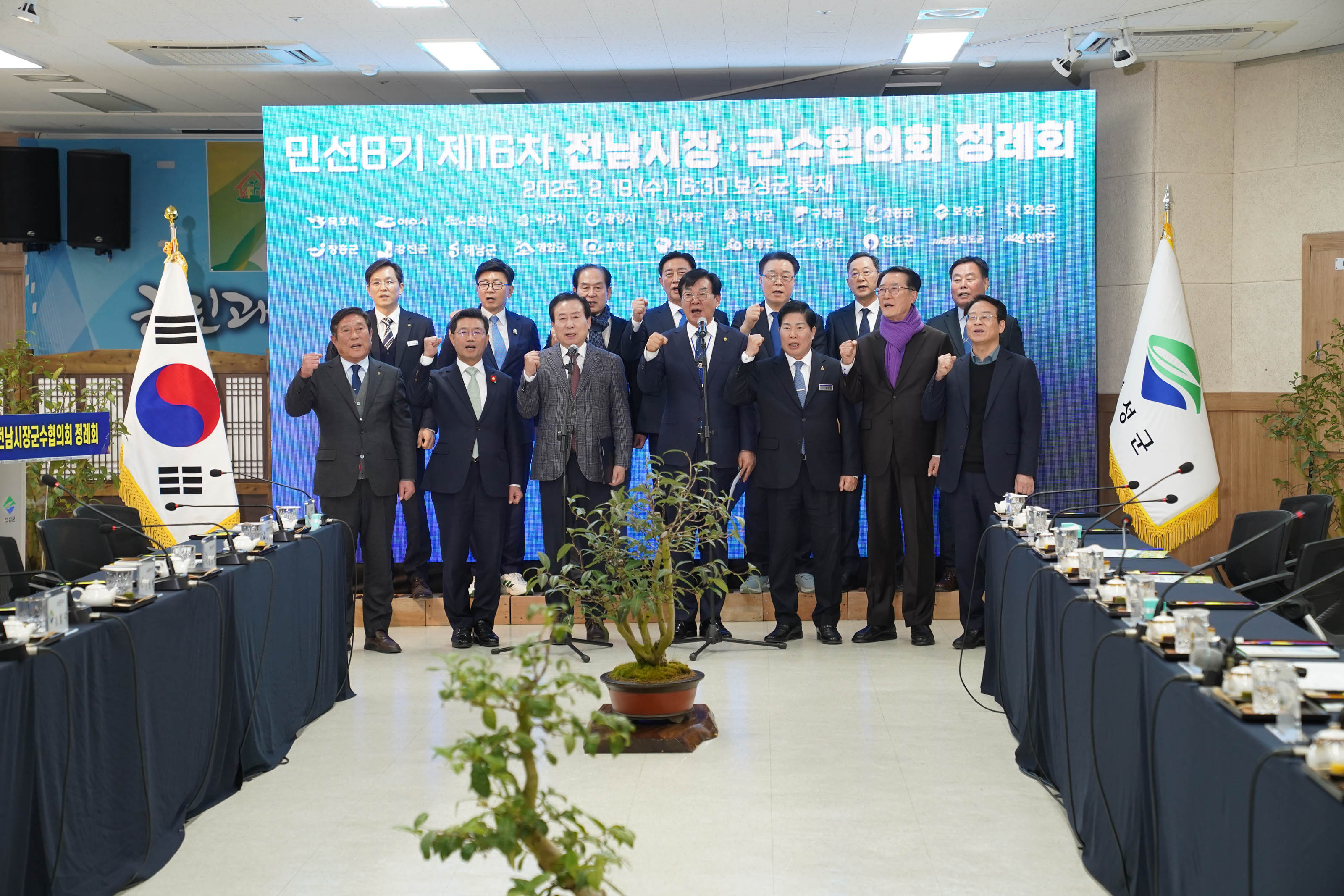 같은 행사장에서 전라남도 시장과 군수들이 주먹을 쥐고 화이팅을 외치며 단체사진을 찍는 장면. LED 배경 화면에 민선8기 제16차 전남시장·군수협의회 정례회 2025.2.19(수) 16:30 보성군 봇재라는 문구가 선명하게 보이고, 양쪽 테이블에는 회의 자료와 음료 등이 정돈되어 있음.