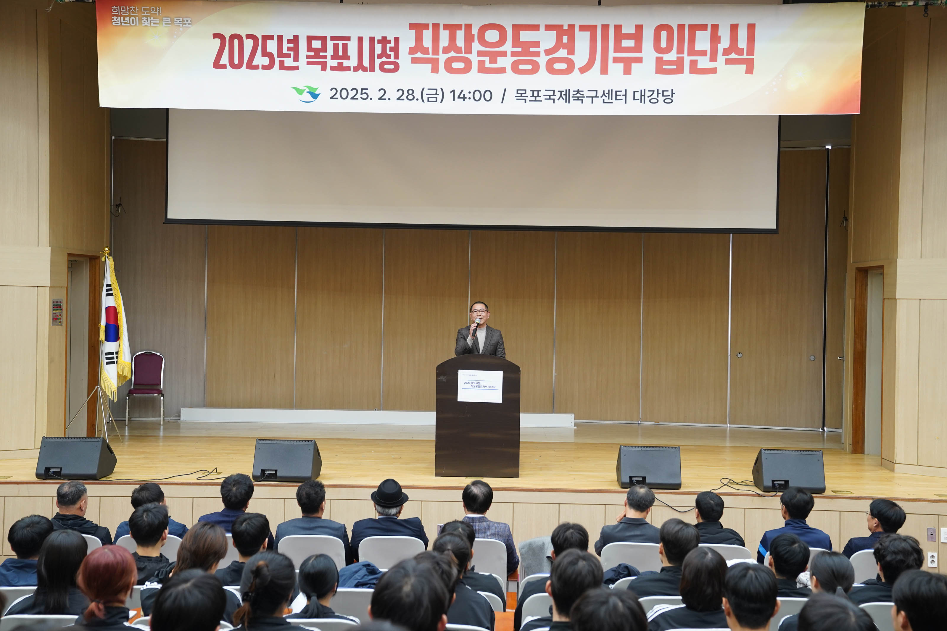 ‘2025년 목포시청 직장운동경기부 입단식 2025.2.28(금) 14:00 / 목포국제축구센터 대강당’ 현수막 아래에서 또 다른 관계자가 연설 중인 모습.