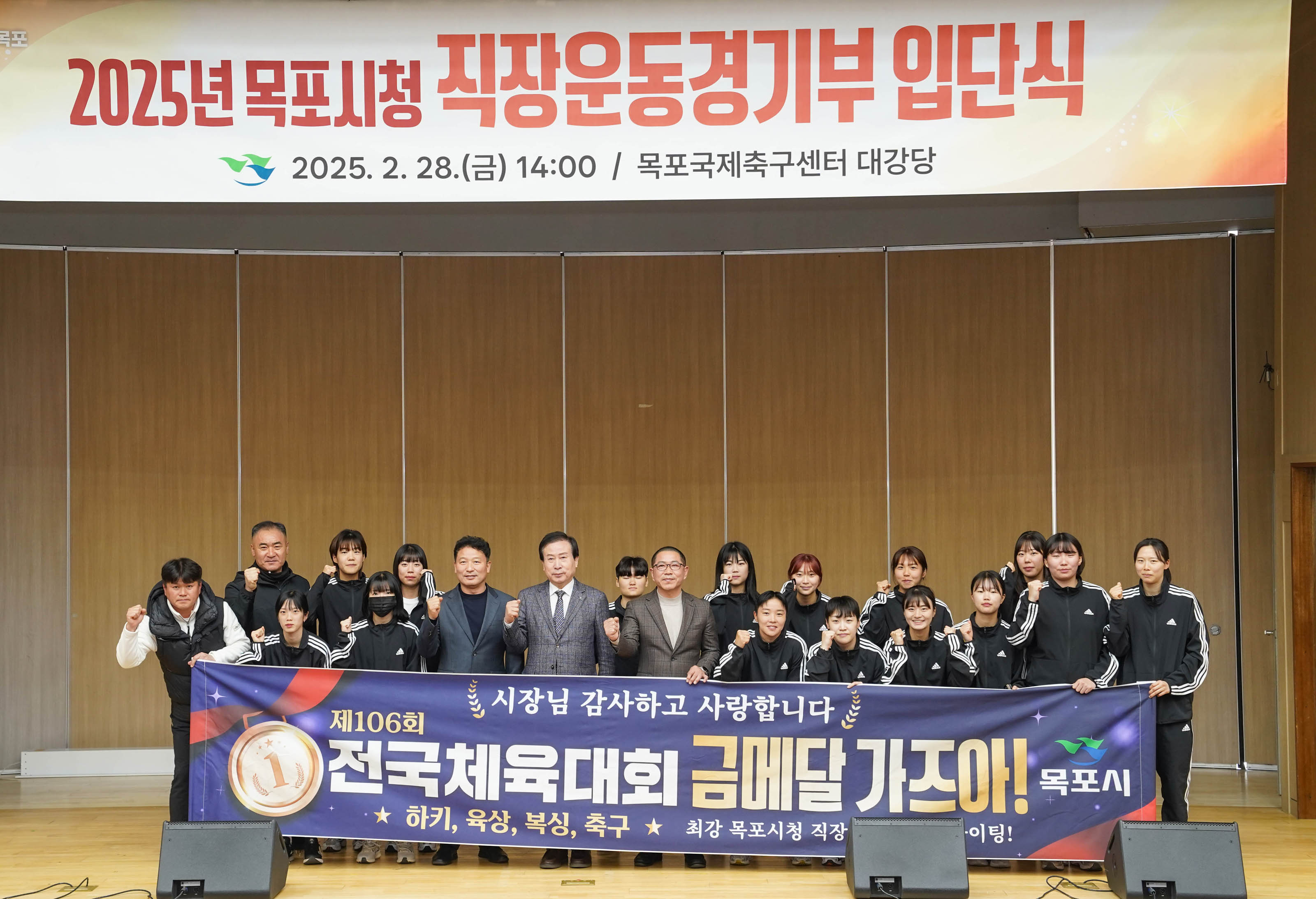 ‘시장님 감사합니다 사랑합니다’, ‘제106회 전국체육대회 금메달 가즈아!’라는 문구가 적힌 대형 현수막을 들고 있는 목포시청 여성 운동선수들과 박홍률 목포시장을 비롯한 관계자들. 현수막 하단에는 ‘하키, 육상, 복싱, 축구 / 최강 목포시청 직장운동경기부 화이팅! 목포시’라는 문구가 적혀 있음.
