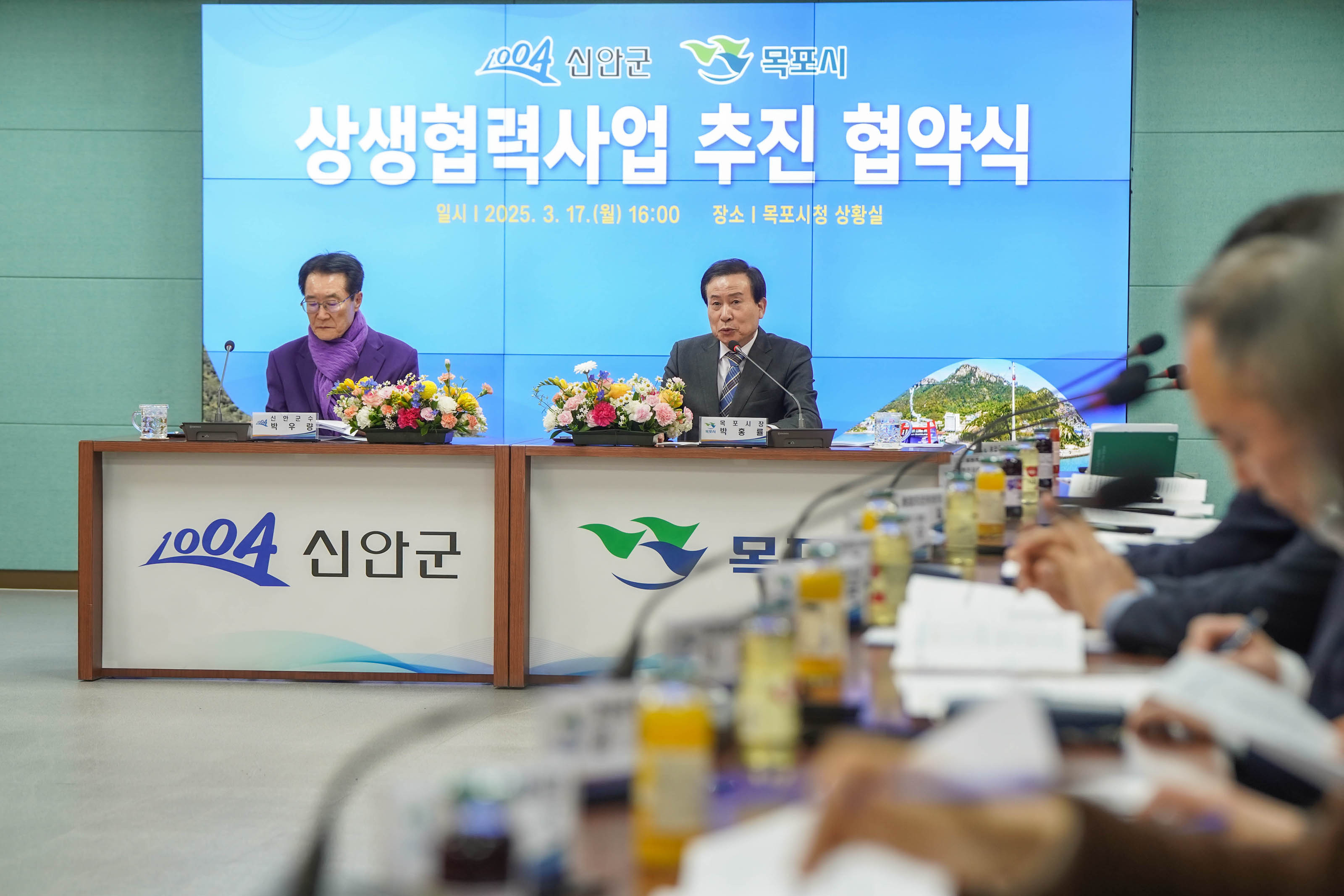 상생협력사업 추진 협약식 회의 테이블에서 박홍률 목포시장이 마이크에 얘기하는 모습. 회의에 참여한 다른 관계자들은 얘기를 듣고 있다. 뒷배경의 화면에 '신안군 목포시 상생협력사업 추진 협약식 일시|2025.3.17(월) 16:00 장소| 목포시청 상황실' 이라는 문구가 크게 보인다.