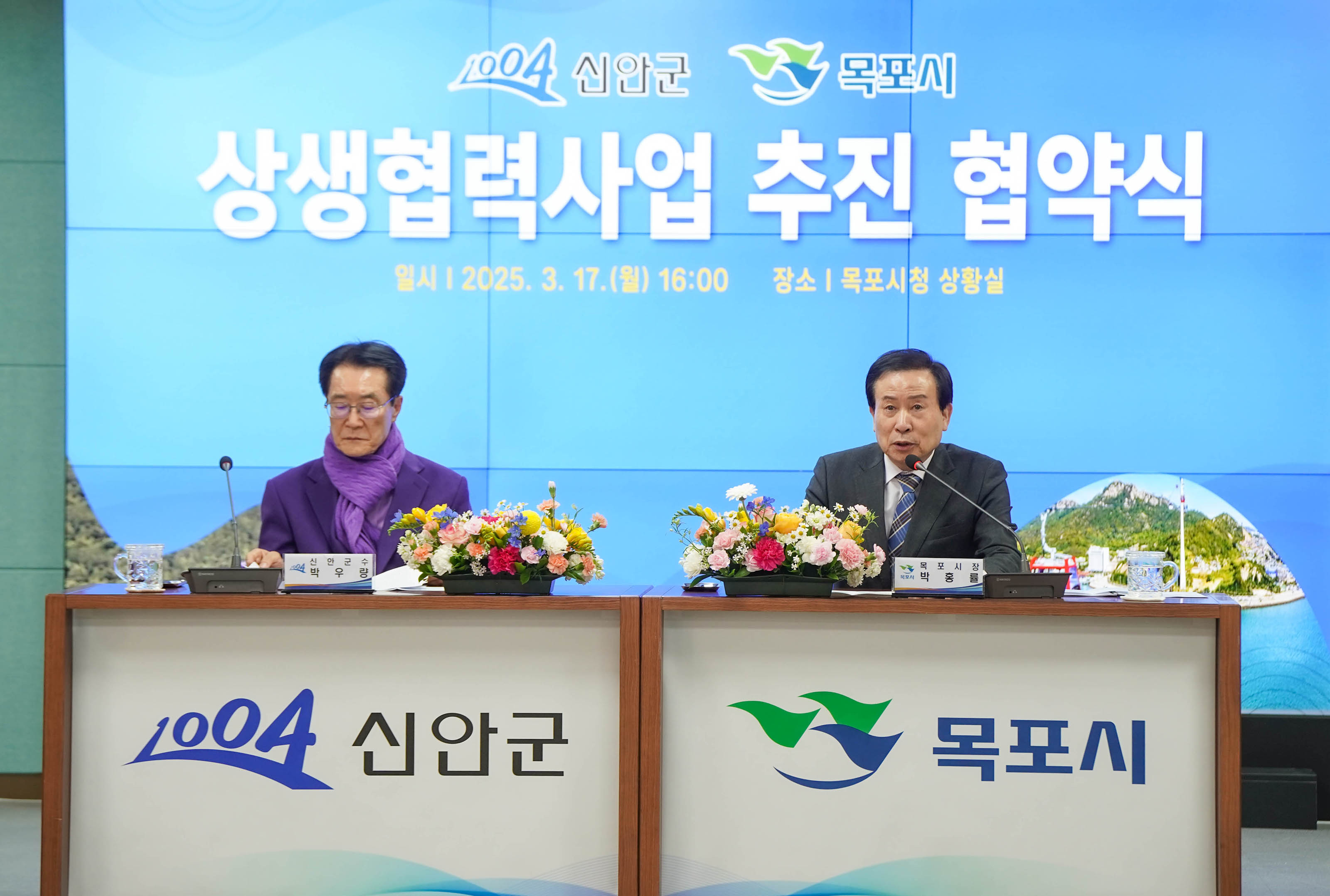 상생협력사업 추진 협약식 회의 테이블에서 박홍률 목포시장이 마이크에 얘기하는 모습. 그 옆에는 보라색 스카프와 자켓을 착용한 관계자가 앉아있고 회의에 참여한 다른 관계자들은 얘기를 듣고 있다. 뒷배경의 화면에 '신안군 목포시 상생협력사업 추진 협약식 일시|2025.3.17(월) 16:00 장소| 목포시청 상황실' 이라는 문구가 크게 보인다.