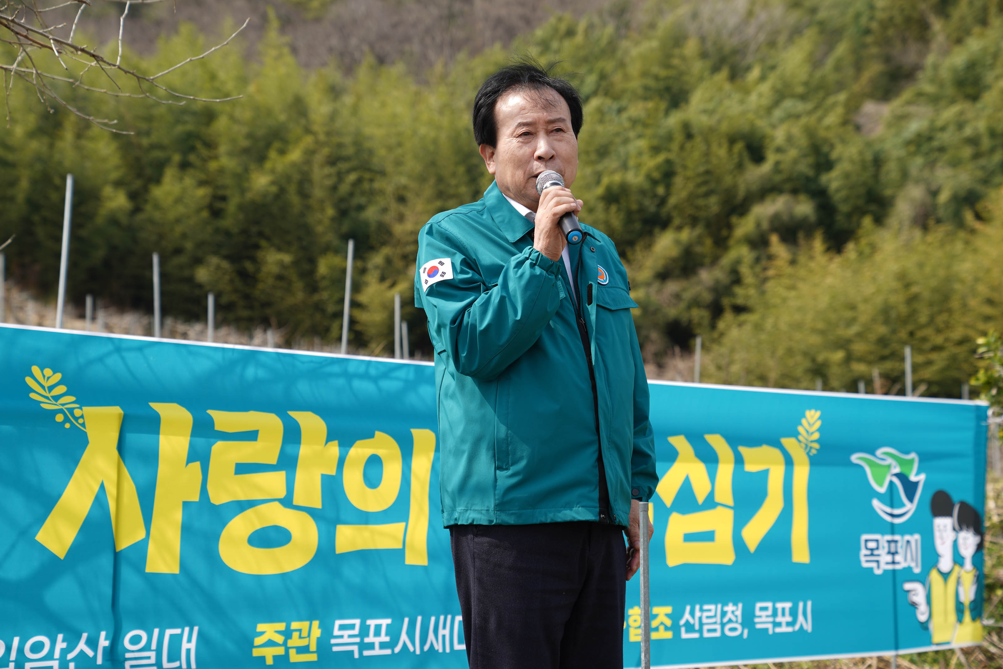 초록색 자켓을 입고 태국기 패치가 달린 자켓을 입은 박홍률 목포시장이 마이크로 연설을 하고 있는 모습. 배경에는