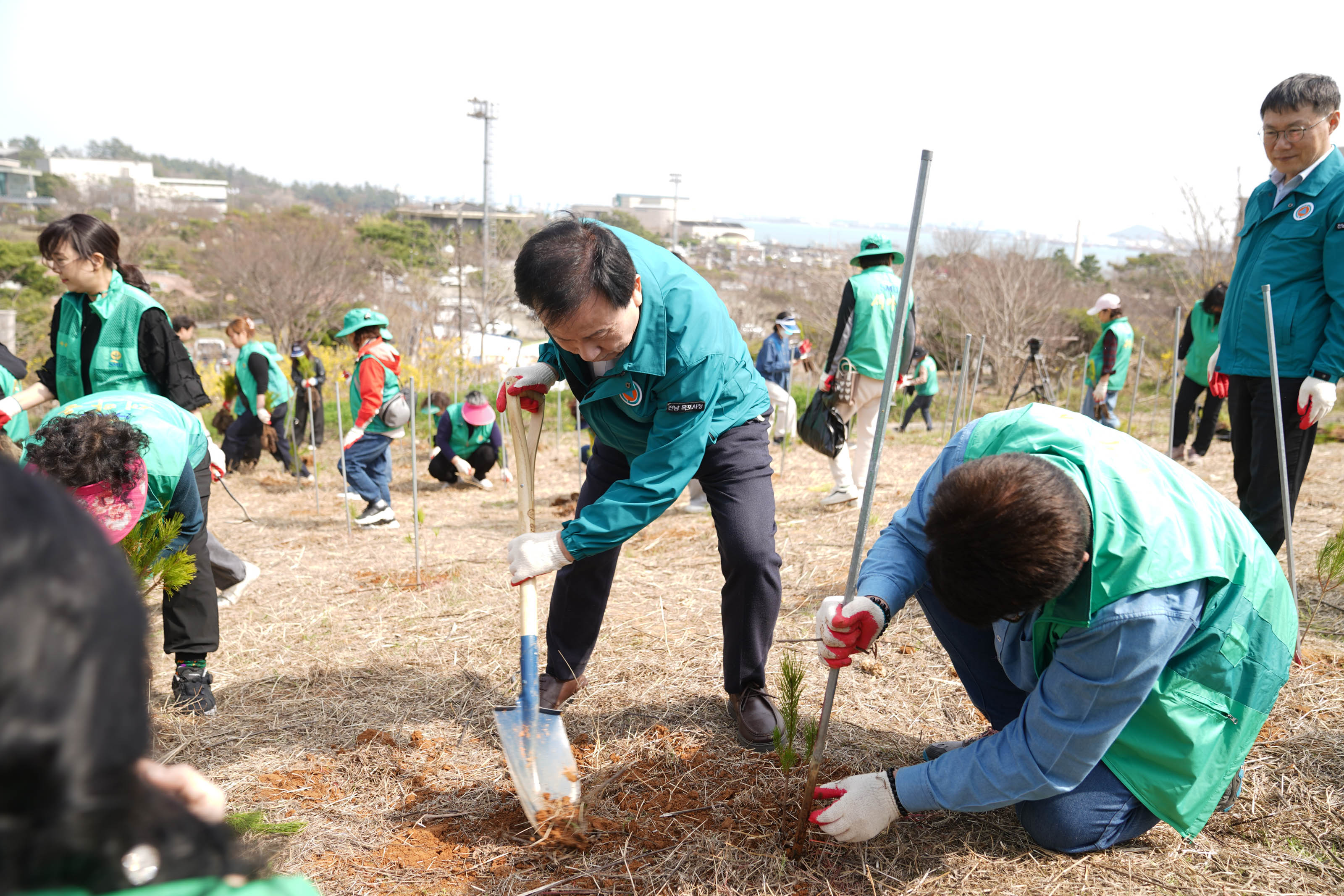 박홍률 목포시장과 한 자원봉사자가 함께 나무를 심고 있는 모습. 배경에는 다른 자원봉사자들도 함께 나무를 심고 있는 모습