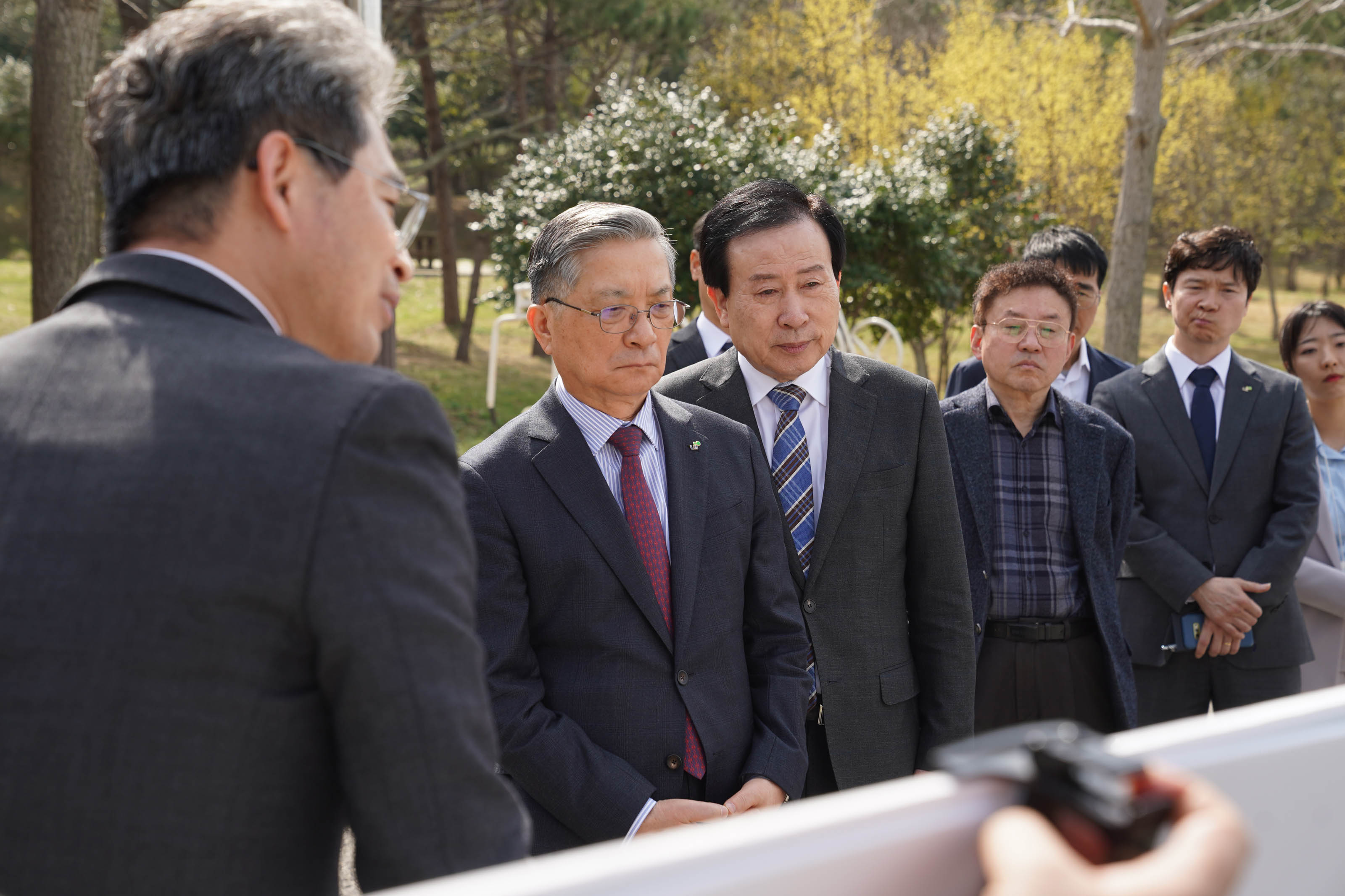 야외에서 양복을 입은 박홍률 목포시장과 이한준 한국주택토지공사 사장이 브리핑을 듣고 있다. 가운데 인물들은 진지한 표정으로 화이트보드를 바라보고 있으며, 주변에 다른 관계자들이 서 있다.